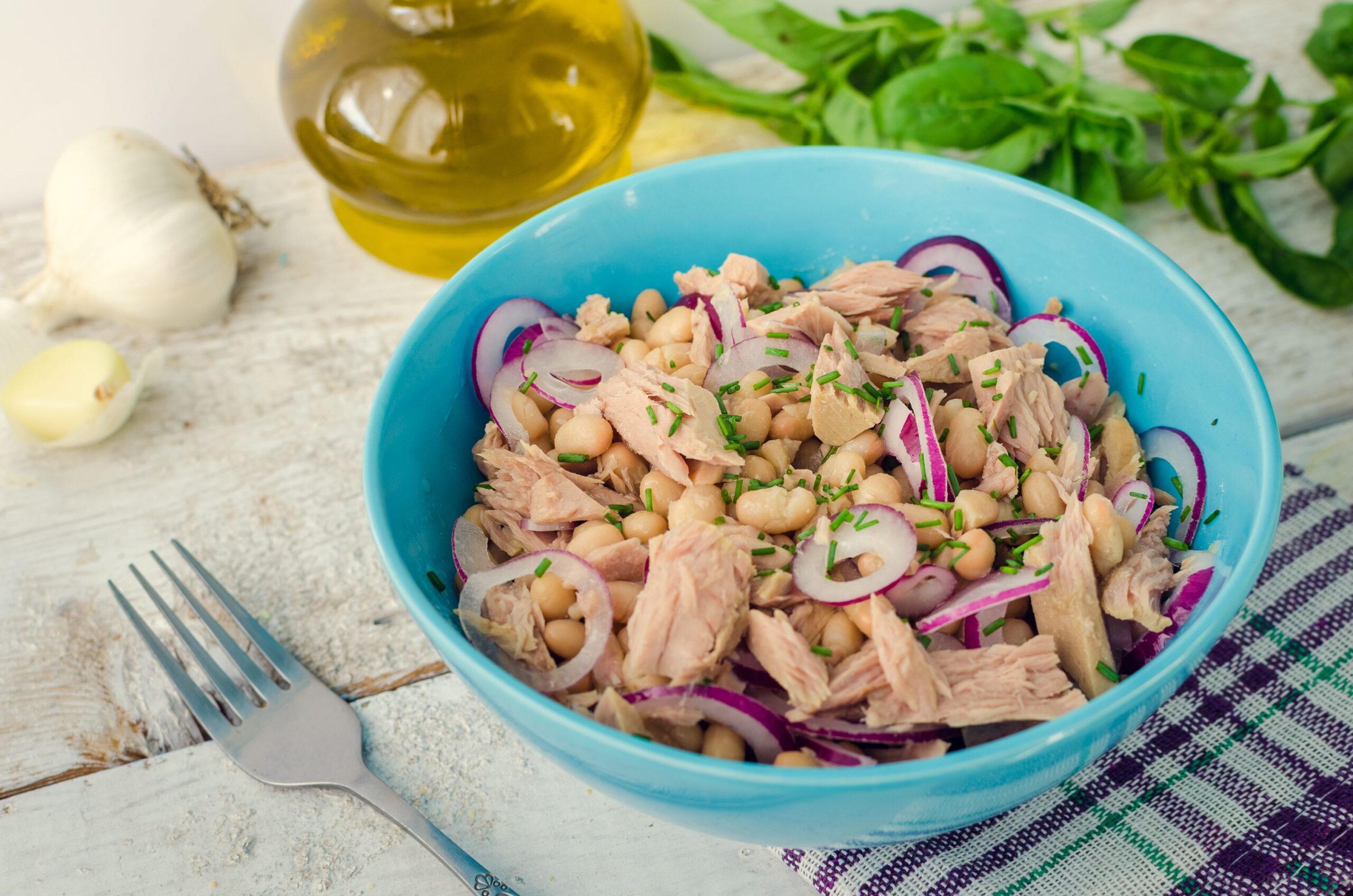 Tuna salad with white beans and red onions in a bowl with basil leaves on white old wooden background. Rustic style. Italian cuisine concept. Healthy food. Selective focus.