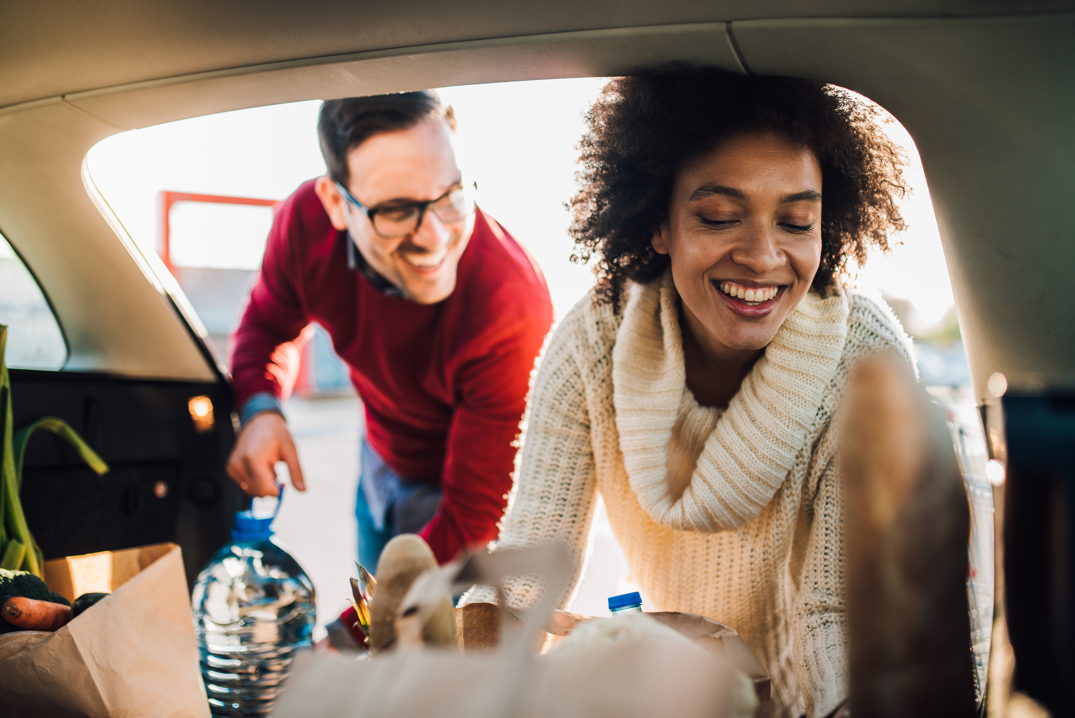 Couple Loading Groceries Into Backseat of Car in a Parking Lot of the Grocery Store