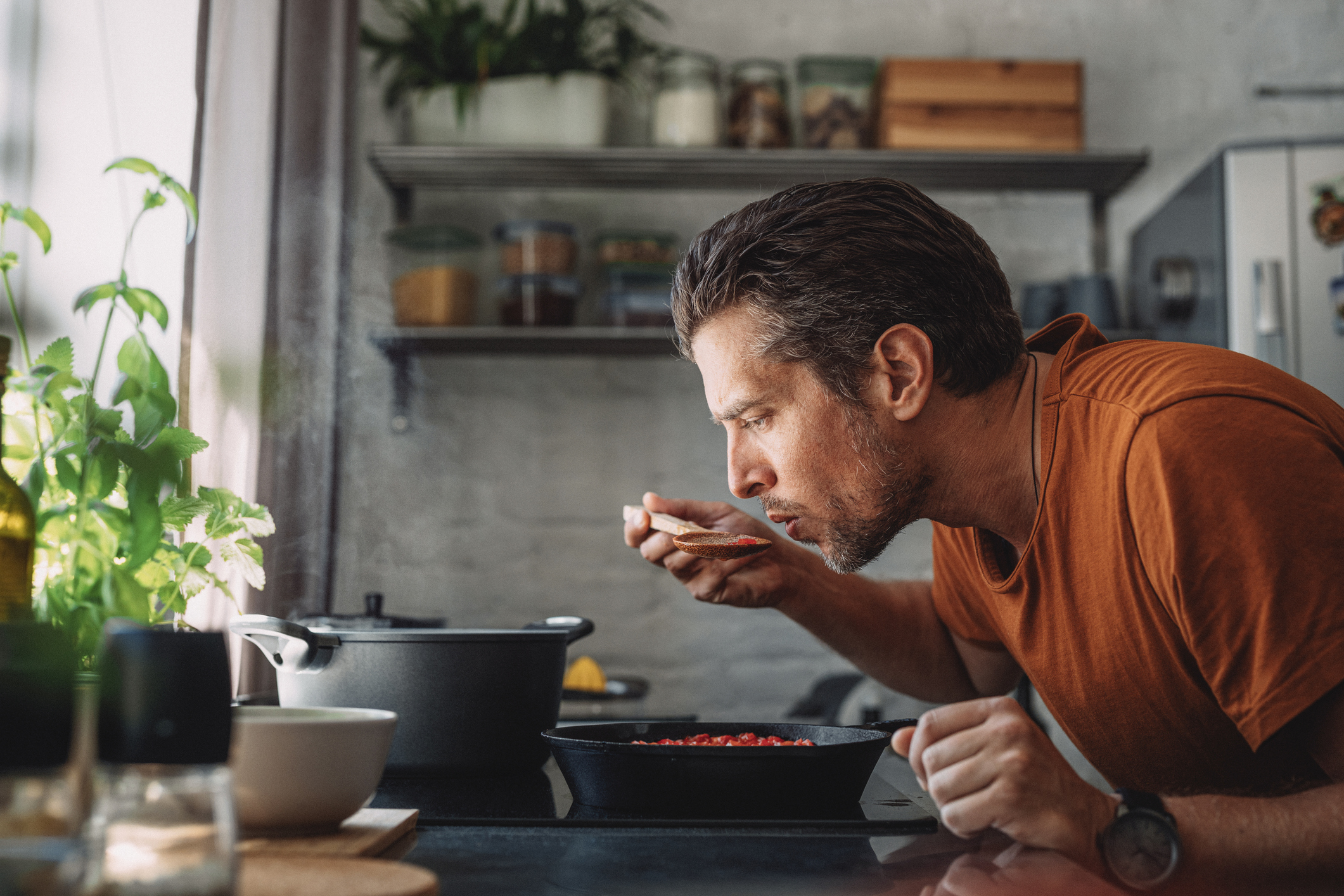 Sideview of Man Close to Skillet, Tasting Contents With a Wooden Spoon in His Kitchen
