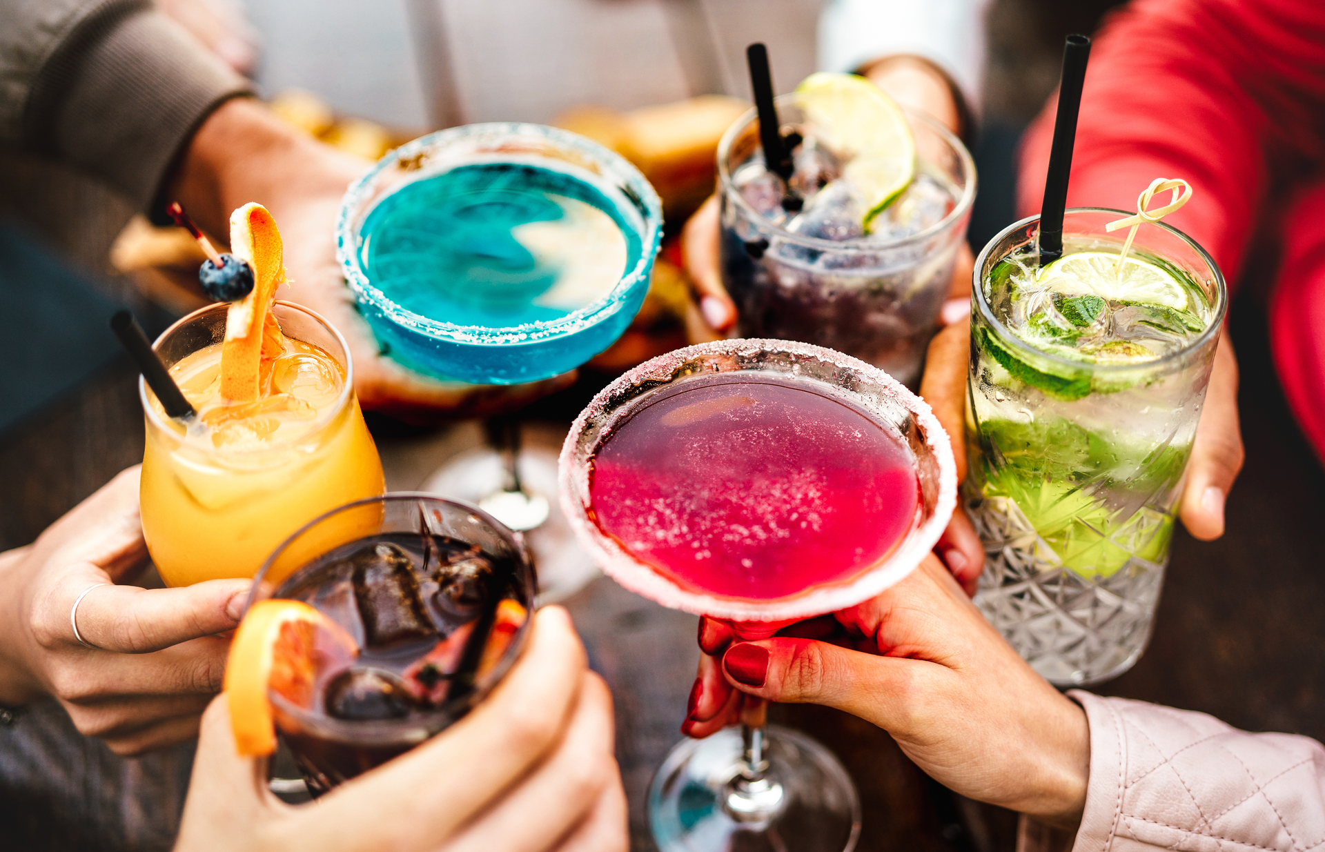 Hands Holding Colorful Cocktails During Happy Hour at a Bar