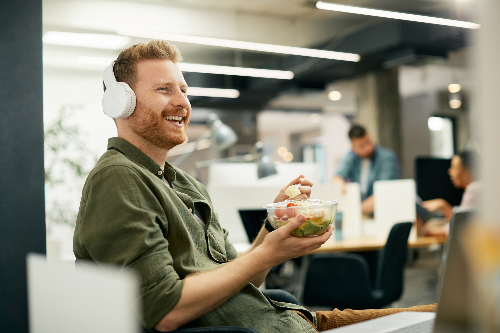 Happy Male Wearing Headphones Eating Lunch at Work
