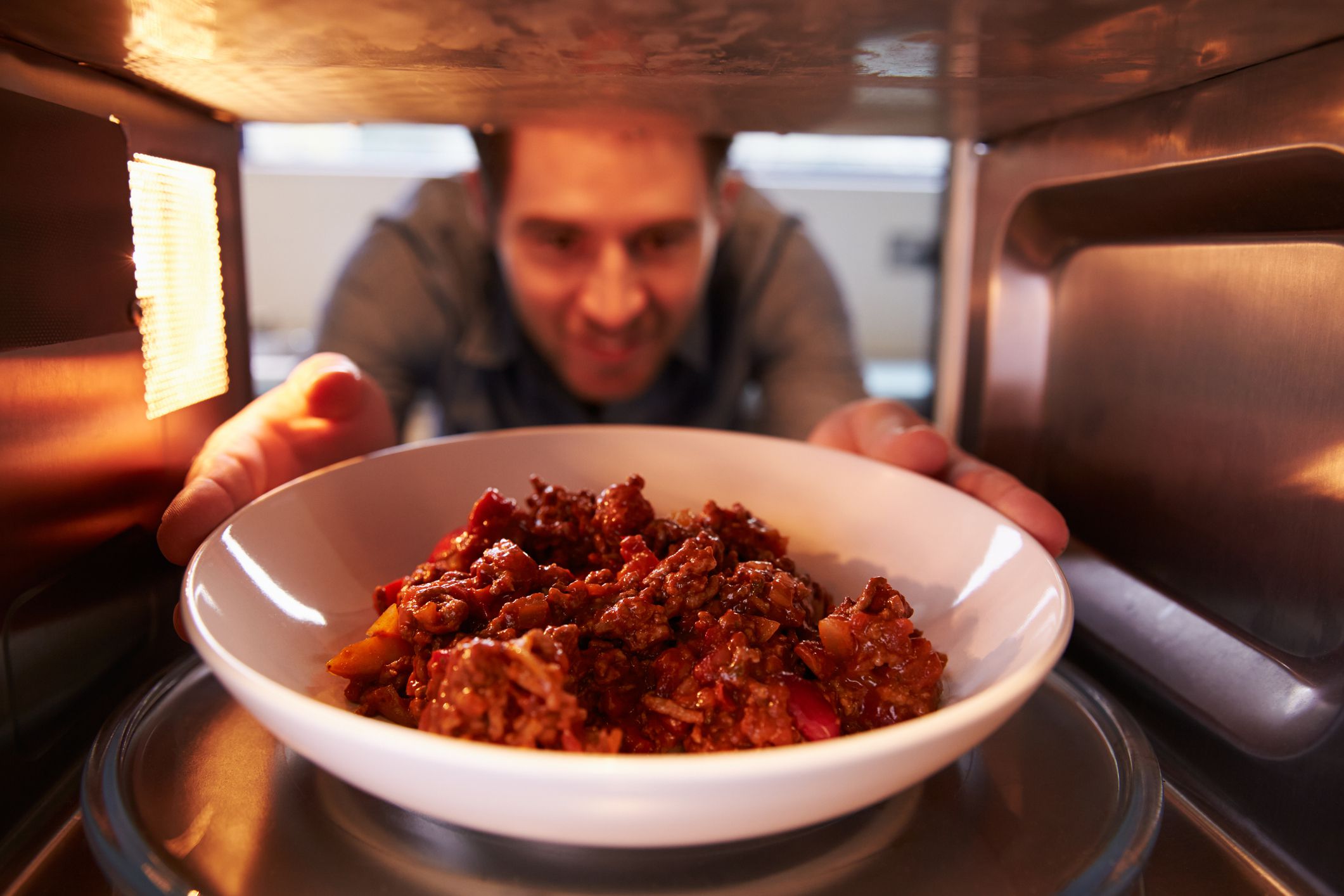 Man Putting Leftover Chili Into Microwave Oven to Cook
