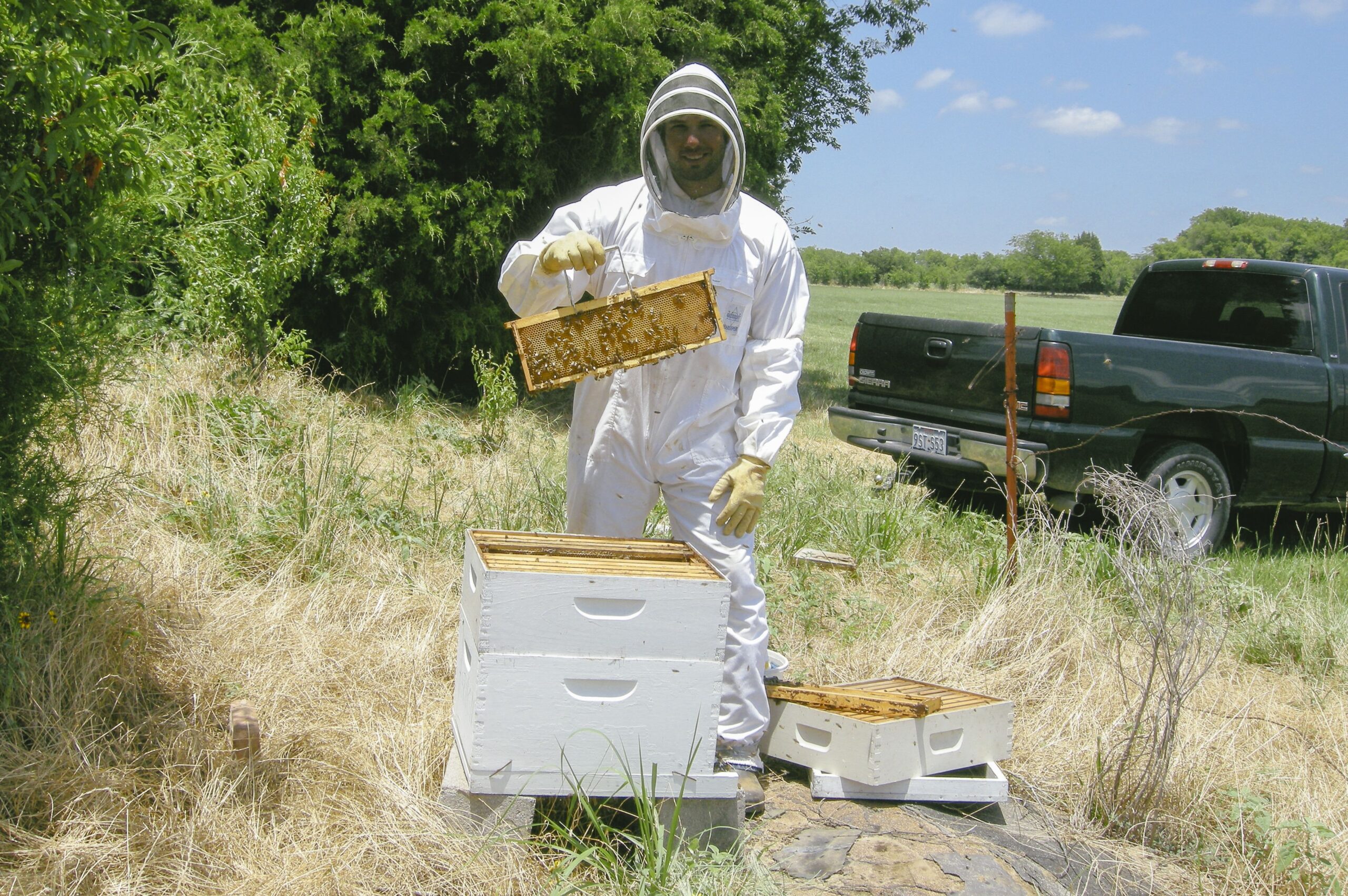 a man beekeeping in a bee suit near a hive