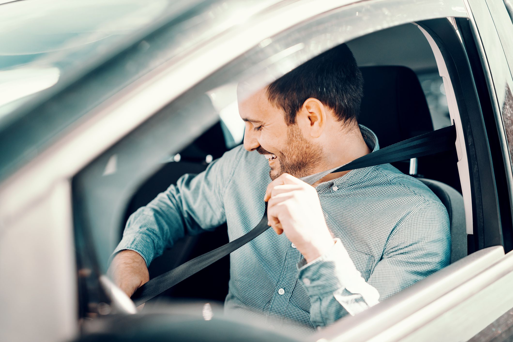 Portrait of smiling Caucasian man fastening seat belt and sitting in his car. Window opened, side view.