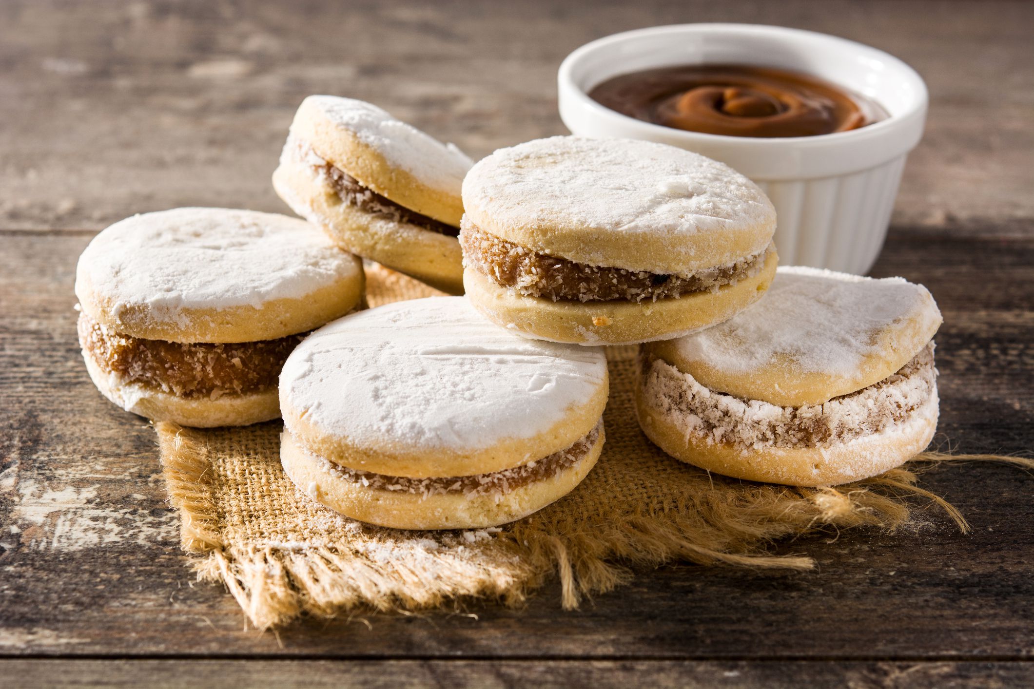 Traditional Argentinian alfajores with dulce de leche and sugar on wooden table.