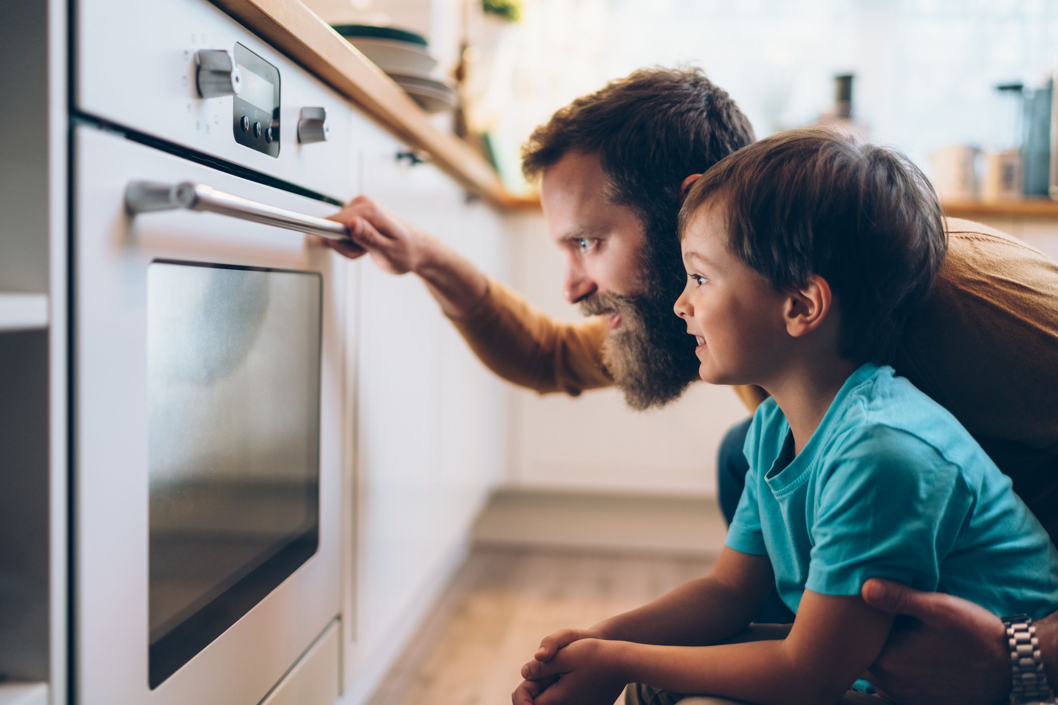 Single father with son baking at home and looking through the oven glass