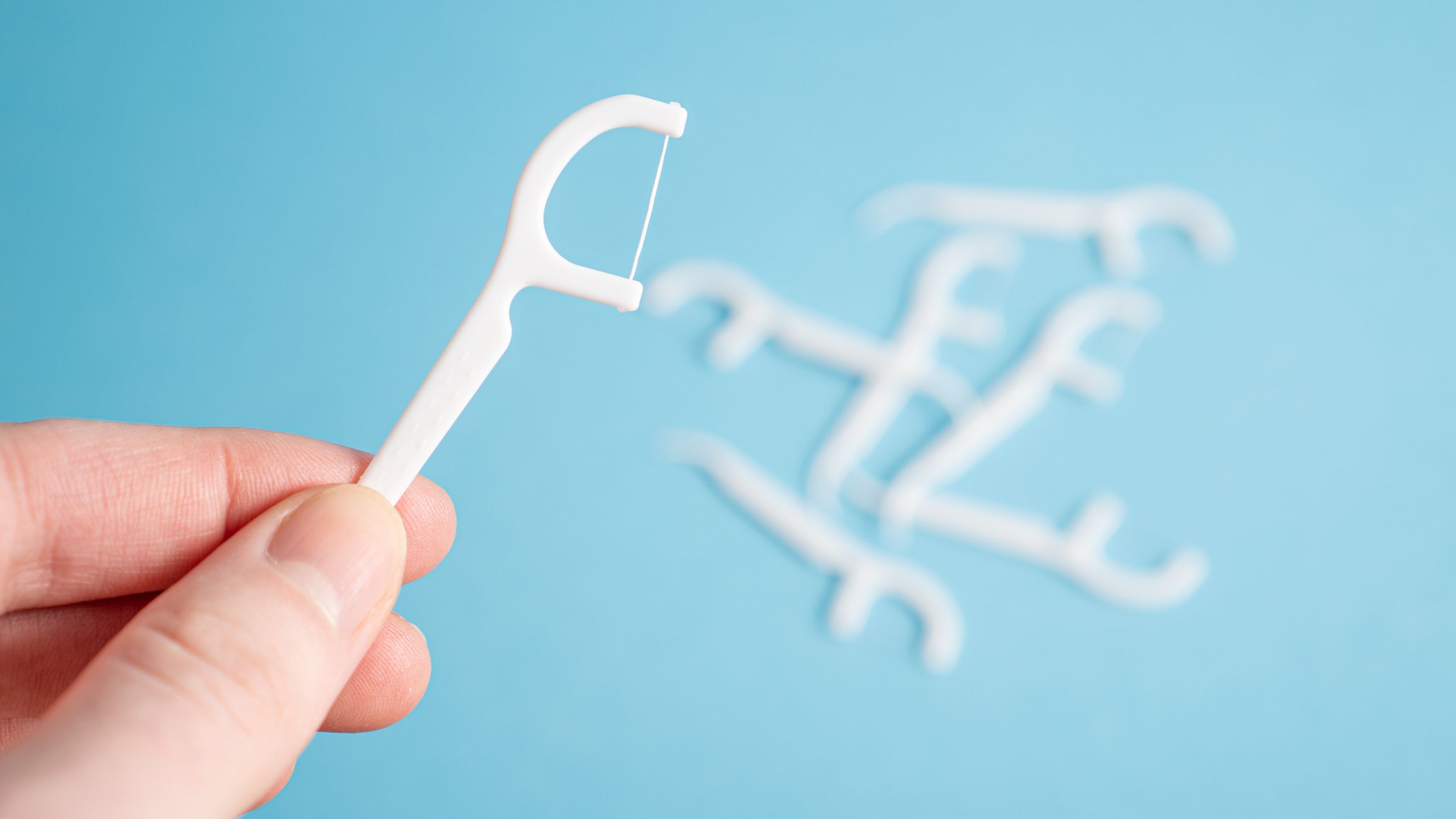Hand holding dental floss pick. Floss stick in hand on blue background. Toothpick. Dental care concept. High quality photo