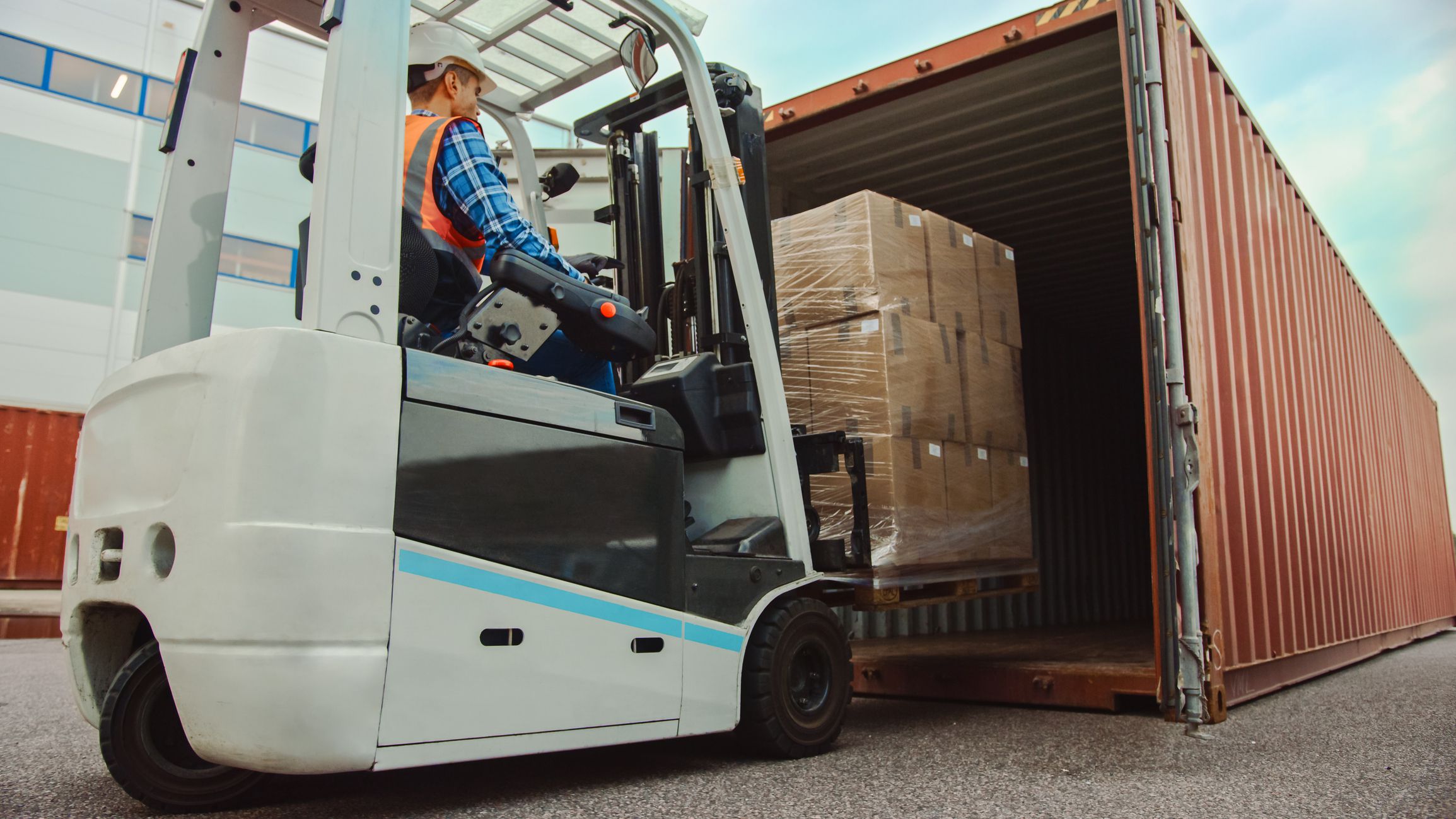 Forklift Driver Loading a Shipping Cargo Container with a Full Pallet with Carboard Boxes in Logistics Operations Port Terminal.