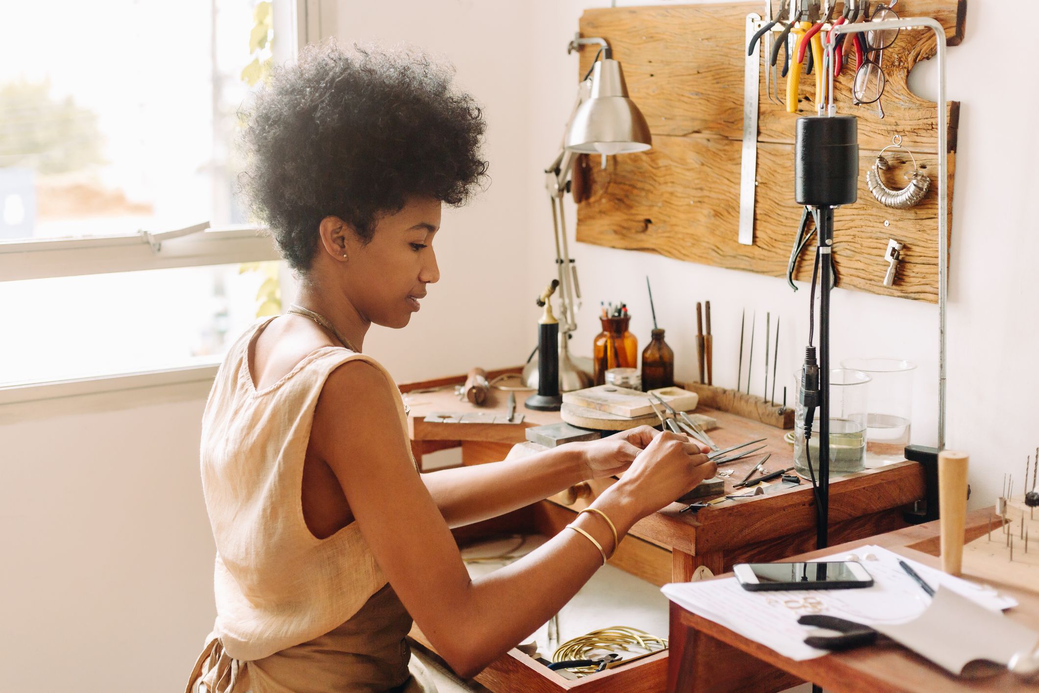 Woman designing jewelry in her workshop. Female artist using traditional tools for making jewelry in her studio.