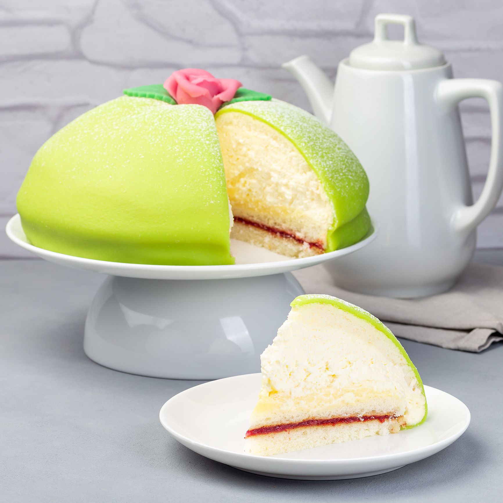Slice of traditional Swedish dessert Princess cake with green marzipan cover and pink rose decoration, on a gray background, square format