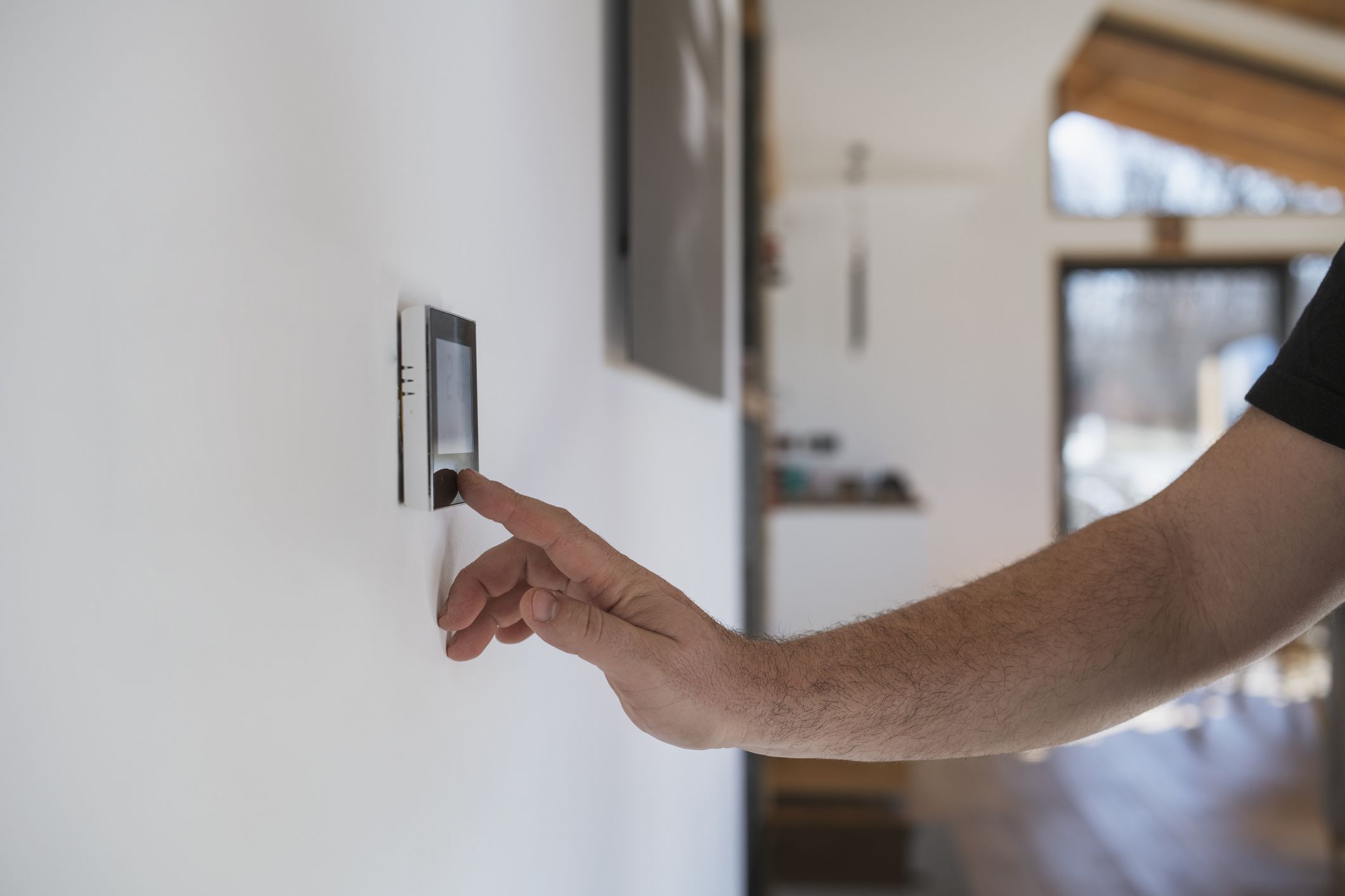 Unrecognisable man at home adjusting thermostat with device on the wall.