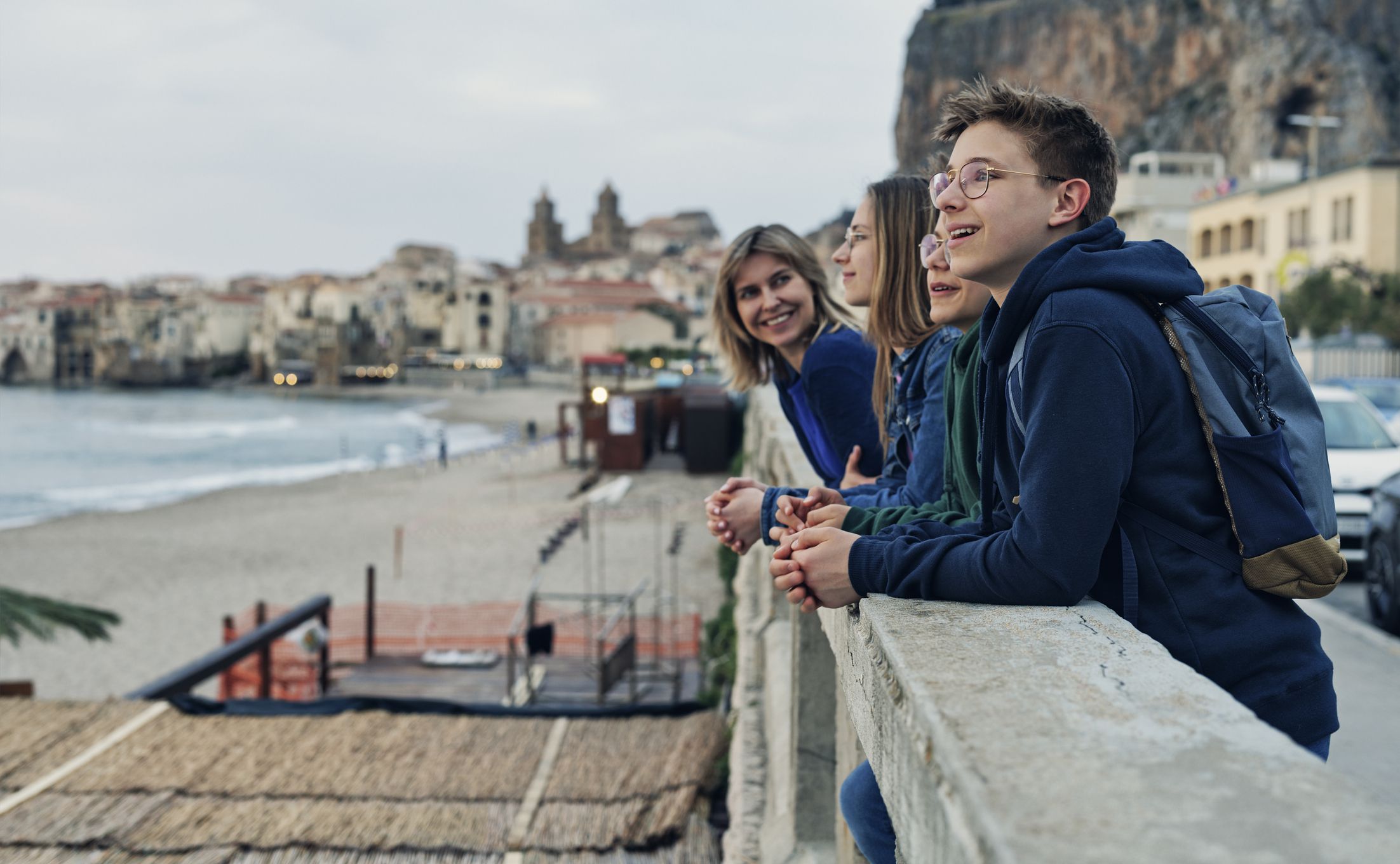 Family sightseeing beautiful Italian town Cefalu in Sicily. Spring, off-season day evening in Italy, Sicily.Mother and three kids are looking at the beautiful view.Canon R5