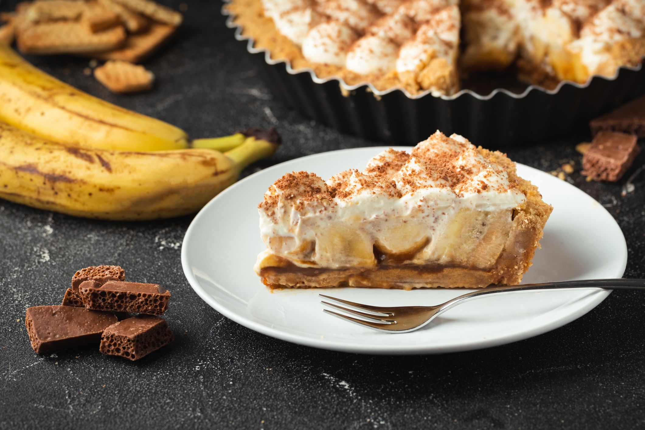 Banoffee cake with banana and caramel sauce filling sprinkled with grated dark chocolate on the black concrete background. English traditional pie