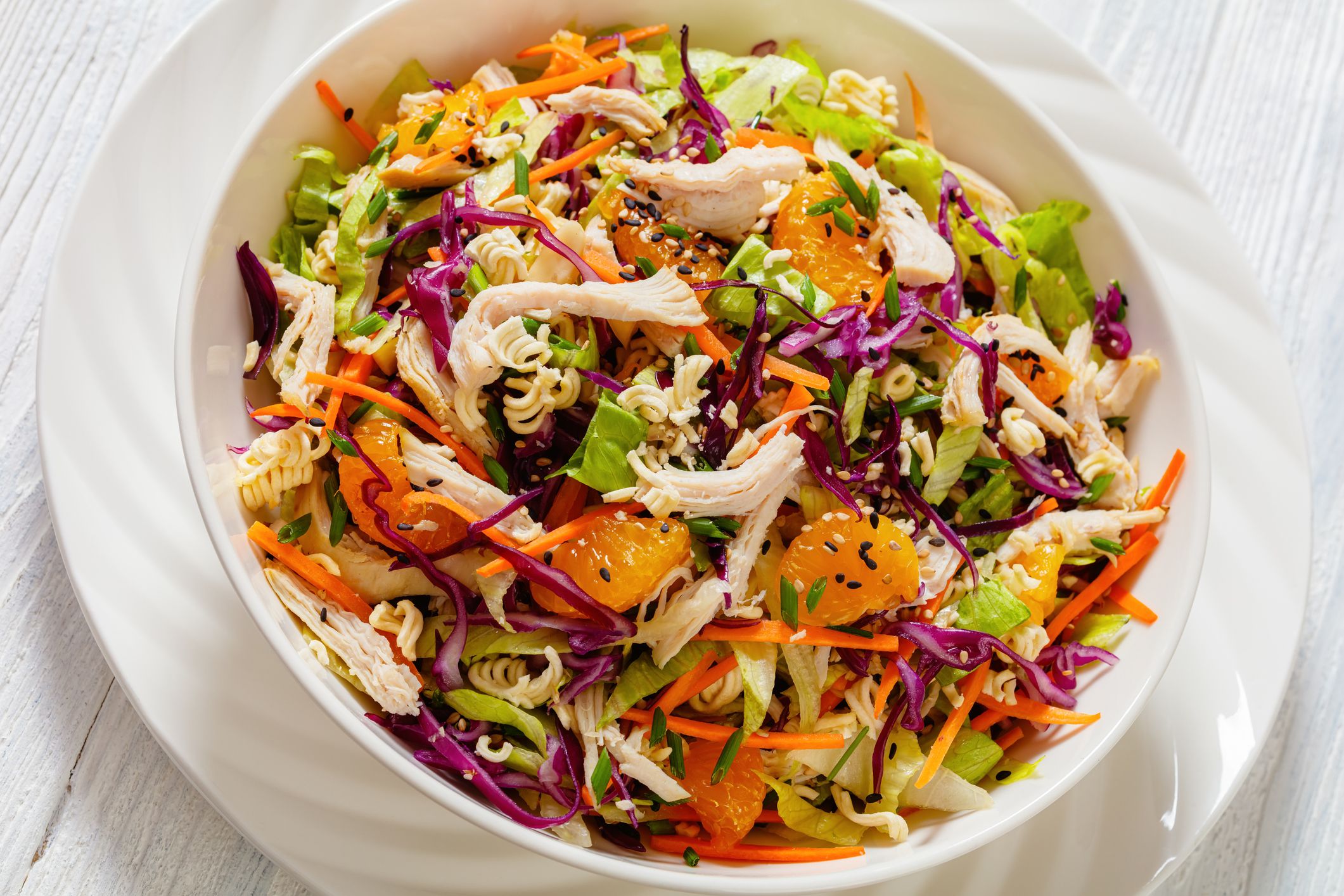 close-up of Chinese Chicken Salad with shredded chicken meat, mandarin oranges, crunchy noodles, red cabbage, napa cabbage, carrots, green onions in bowl