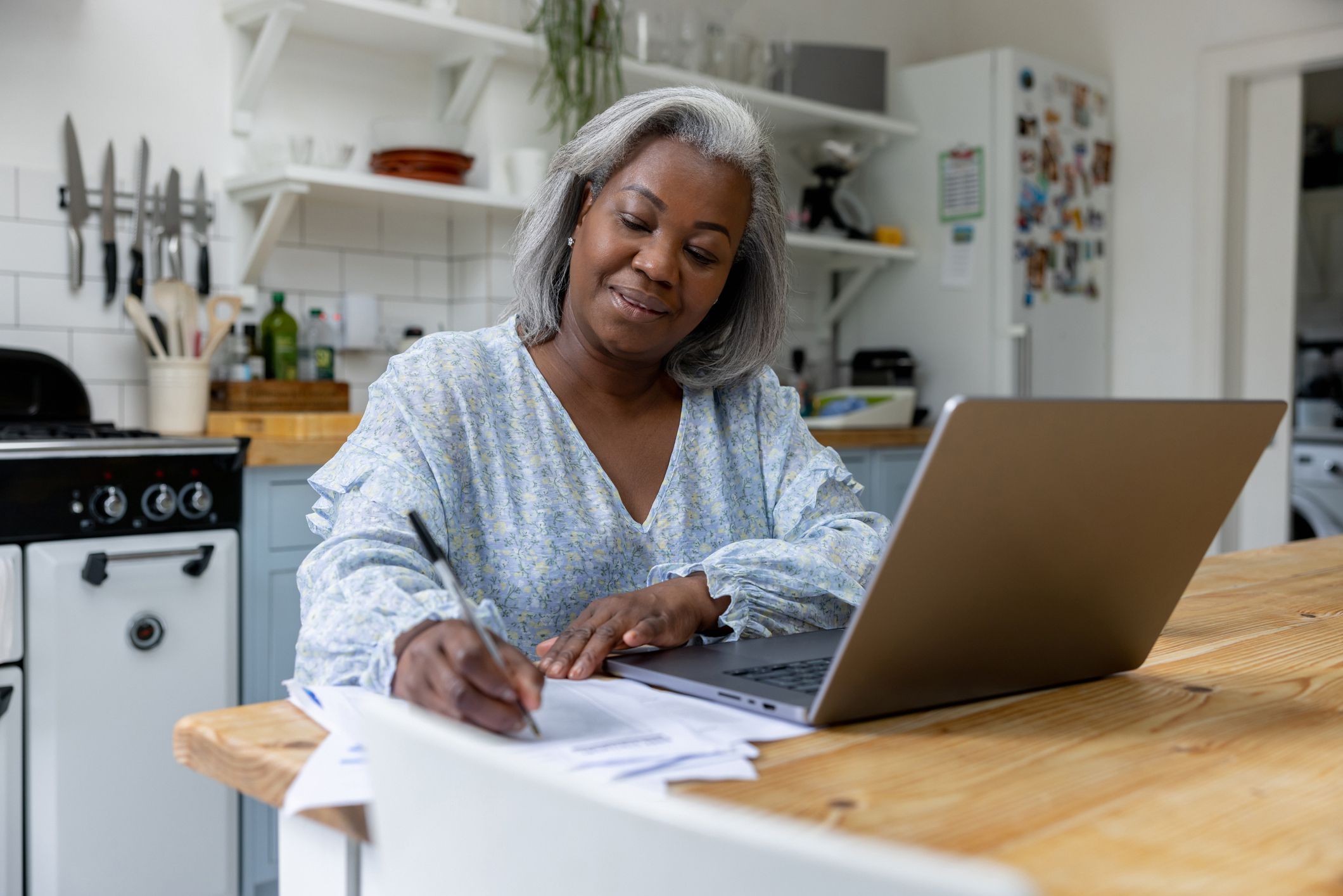 Mature black woman at home taking classes online using her laptop and writing some notes