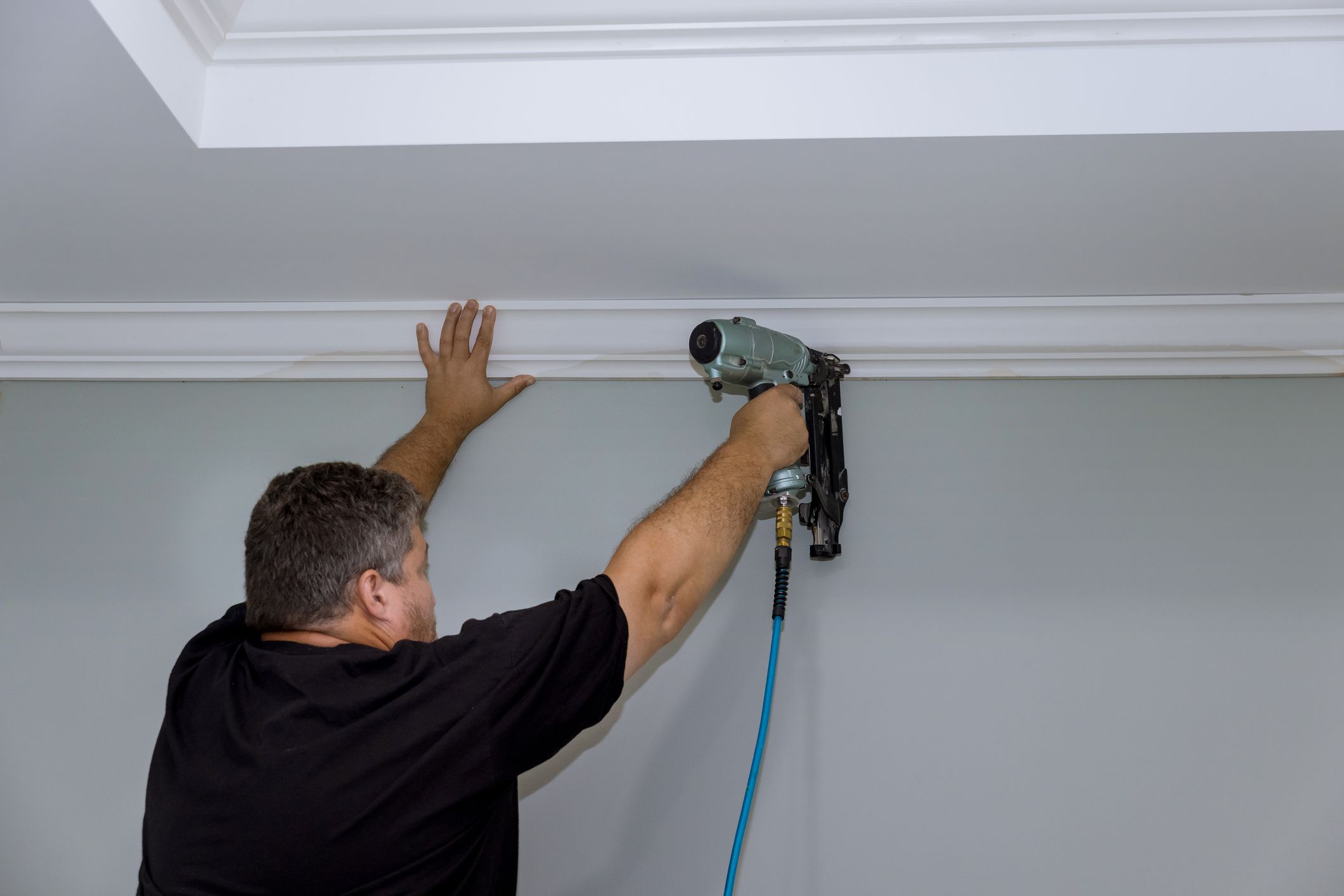 Professional carpenter nails wooden crown molding between the ceiling and the wall in a newly constructed home