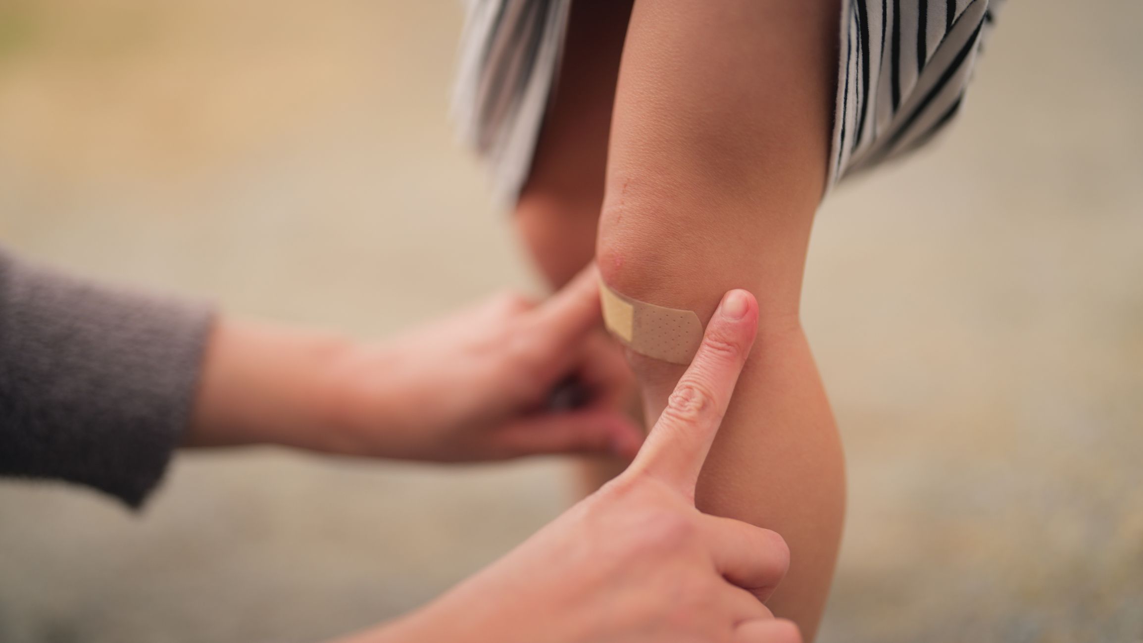 A mother is covering wound of her small daughter with a bandaid in a public park.
