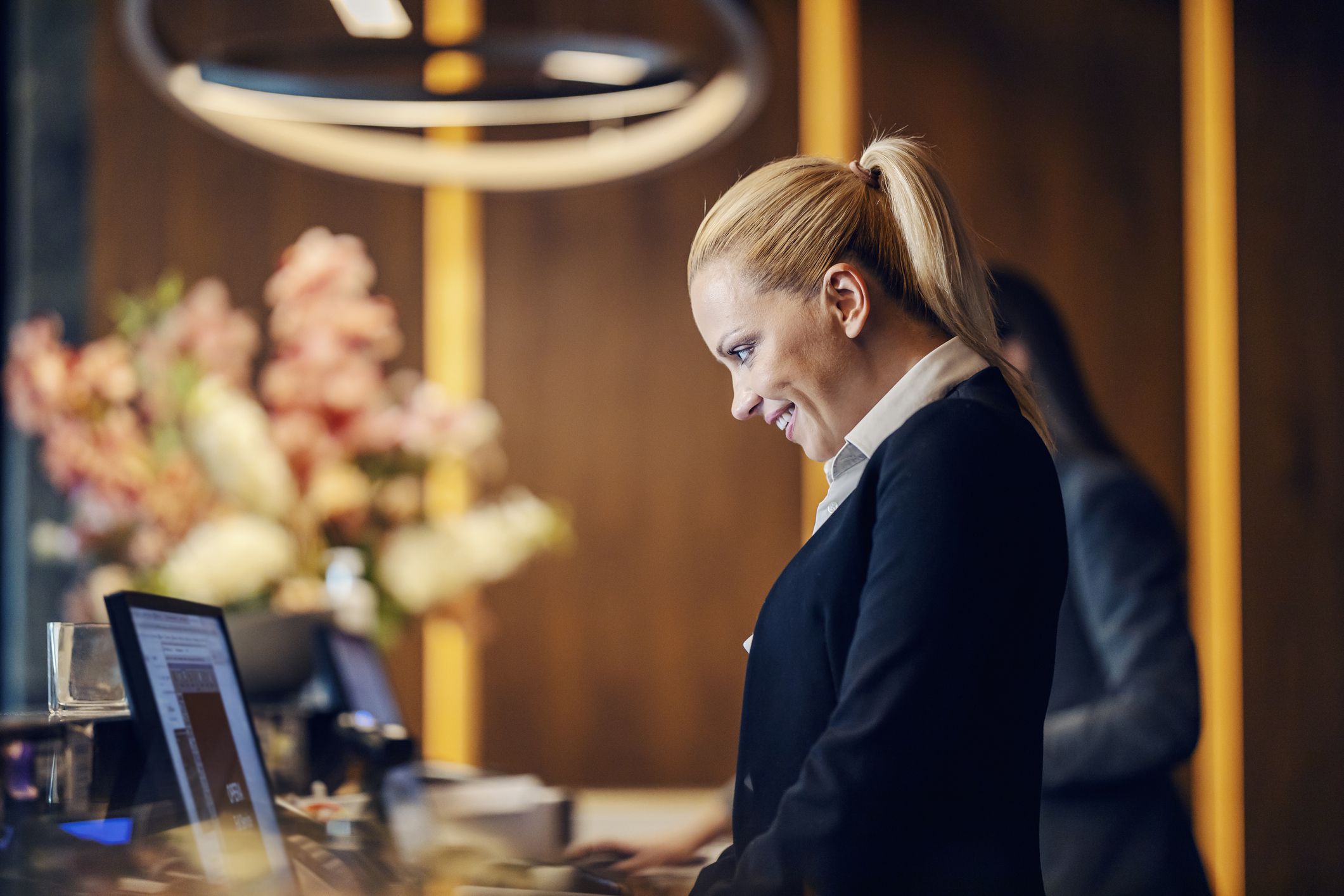 A happy receptionist is making an online reservation on computer while standing at reception.