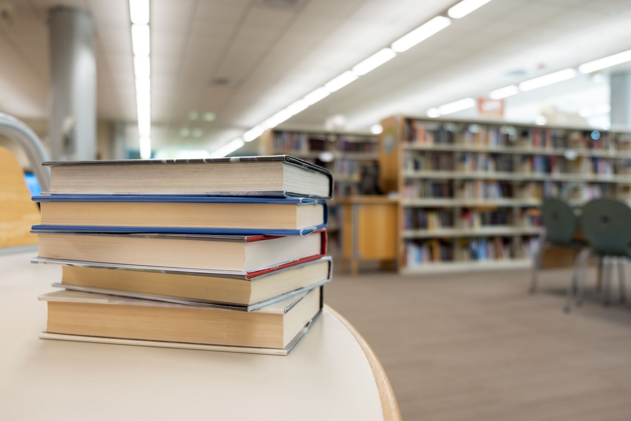 Stack of books on table against bookshelf at library for education, literature or wisdom concept