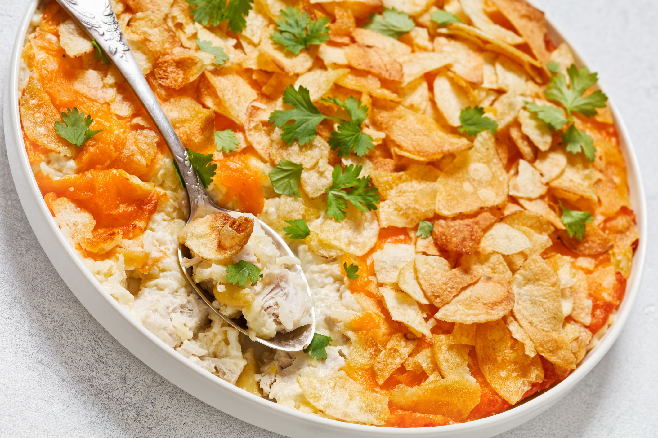 close-up of creamy cheesy chicken almond casserole topped with potato chips in baking dish with spoon, american recipe, dutch angle