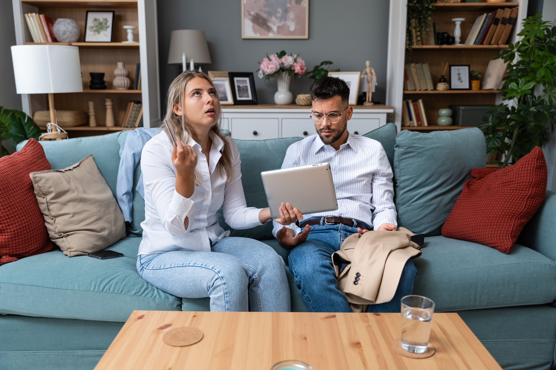 Young couple man and woman argue about overspending money on online shopping, gambling, food delivery. Husband and wife, holding credit card and digital tablet, having issue with home finances.