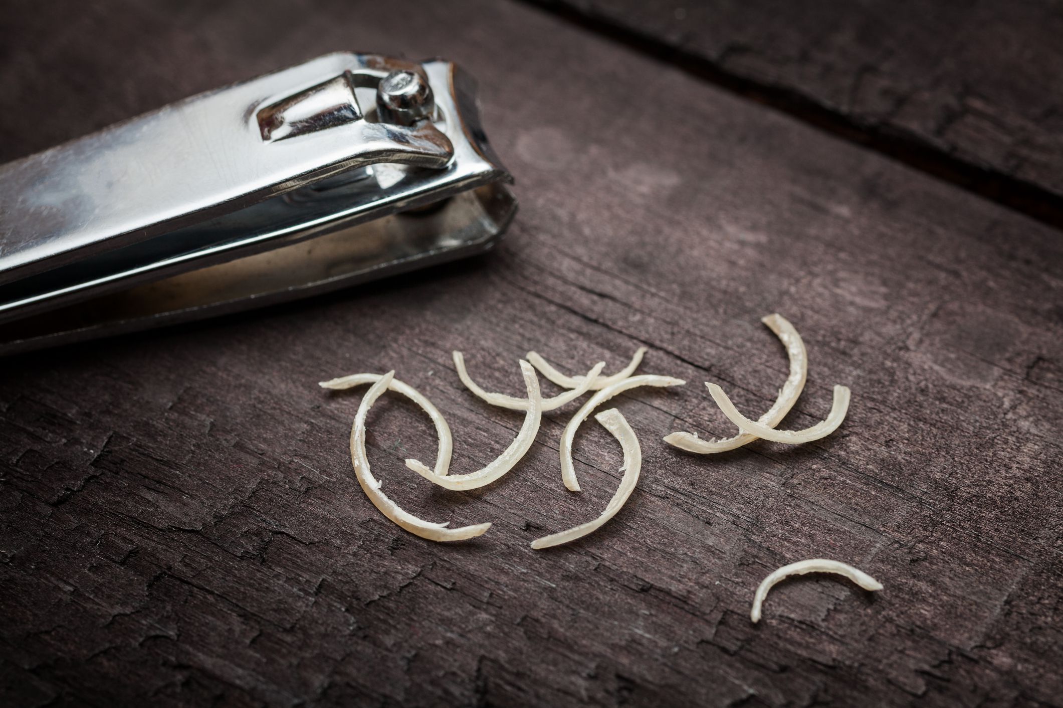 Nail clipper and some nail clippings over a dark wooden surface