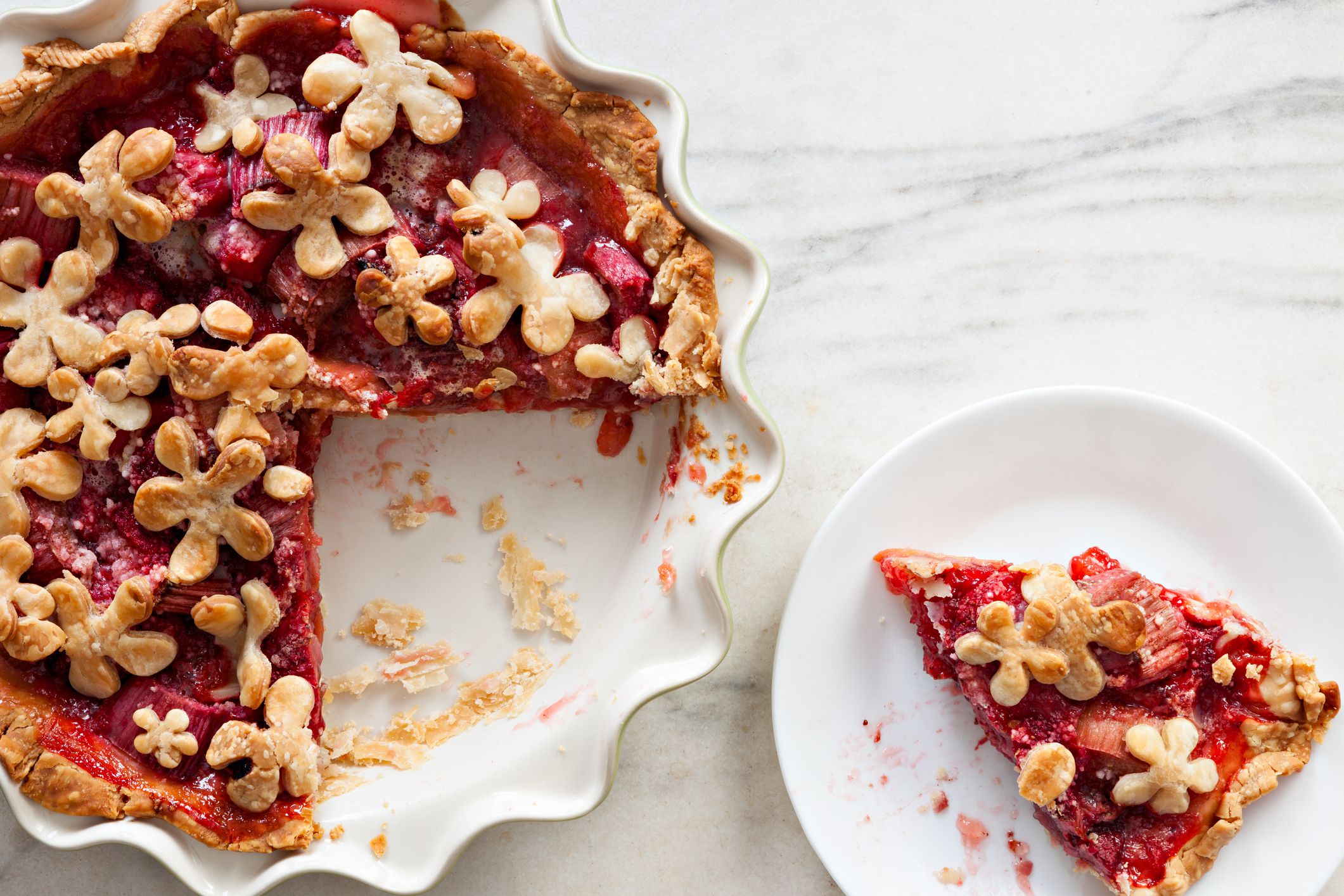 An overhead close up shot of a strawberry rhubarb pie and a slice.