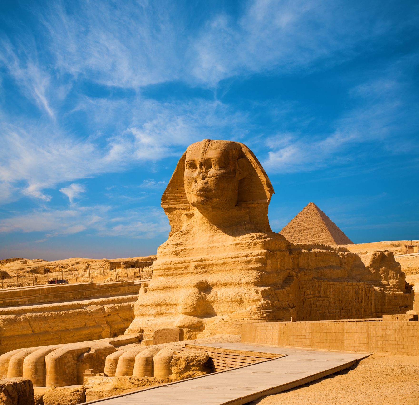 Full length body profile of Great Sphinx including head, feet with great pyramid of Menkaure in background on a clear, blue sky day in Giza, Egypt empty with no people. Copy space