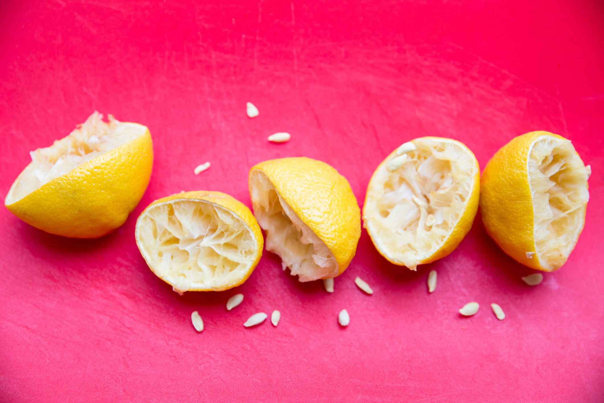 Sliced and squeezed lemons with seeds on a red cutting board