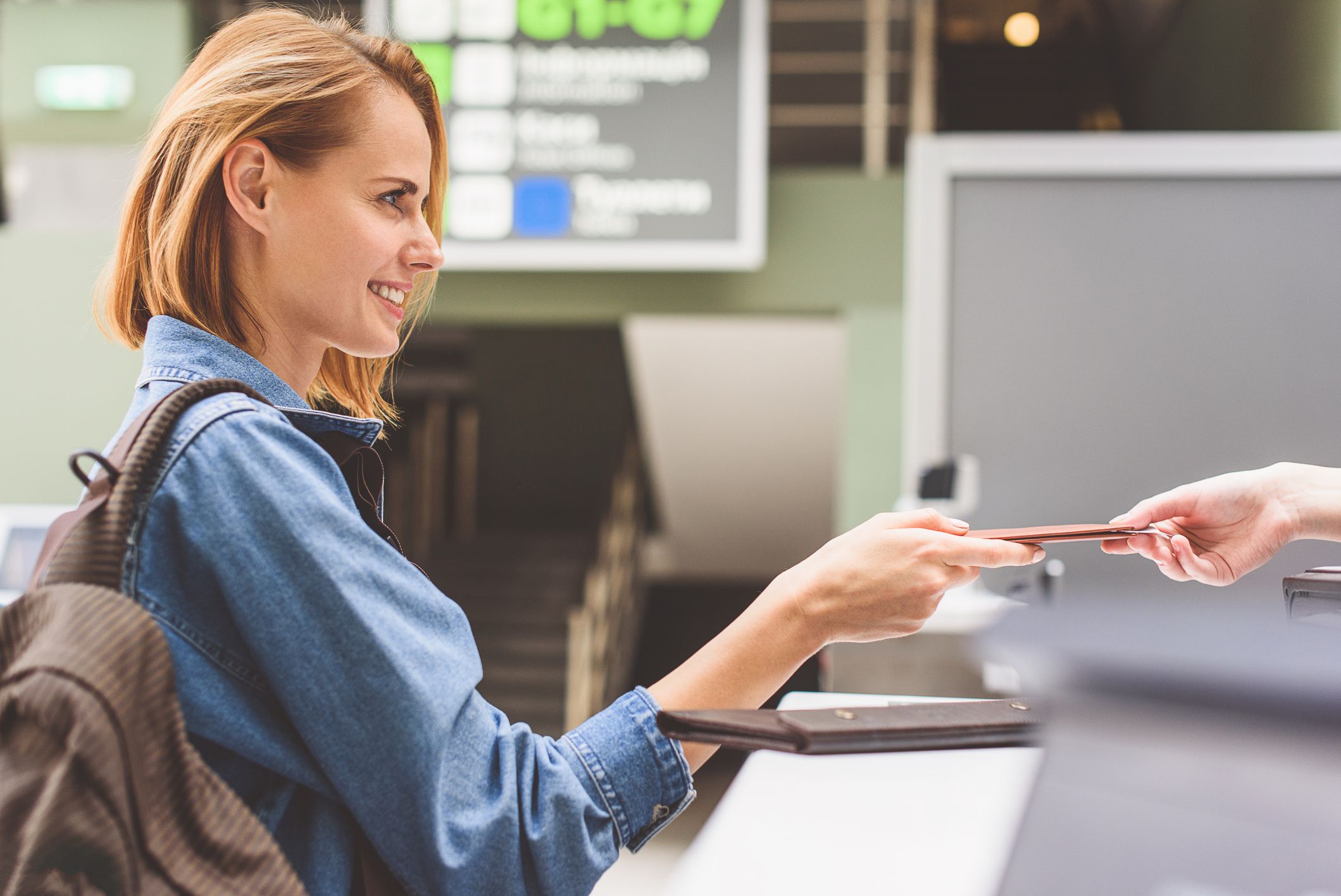 Excited young woman is showing her documents to check-in attendant. She is standing and smiling
