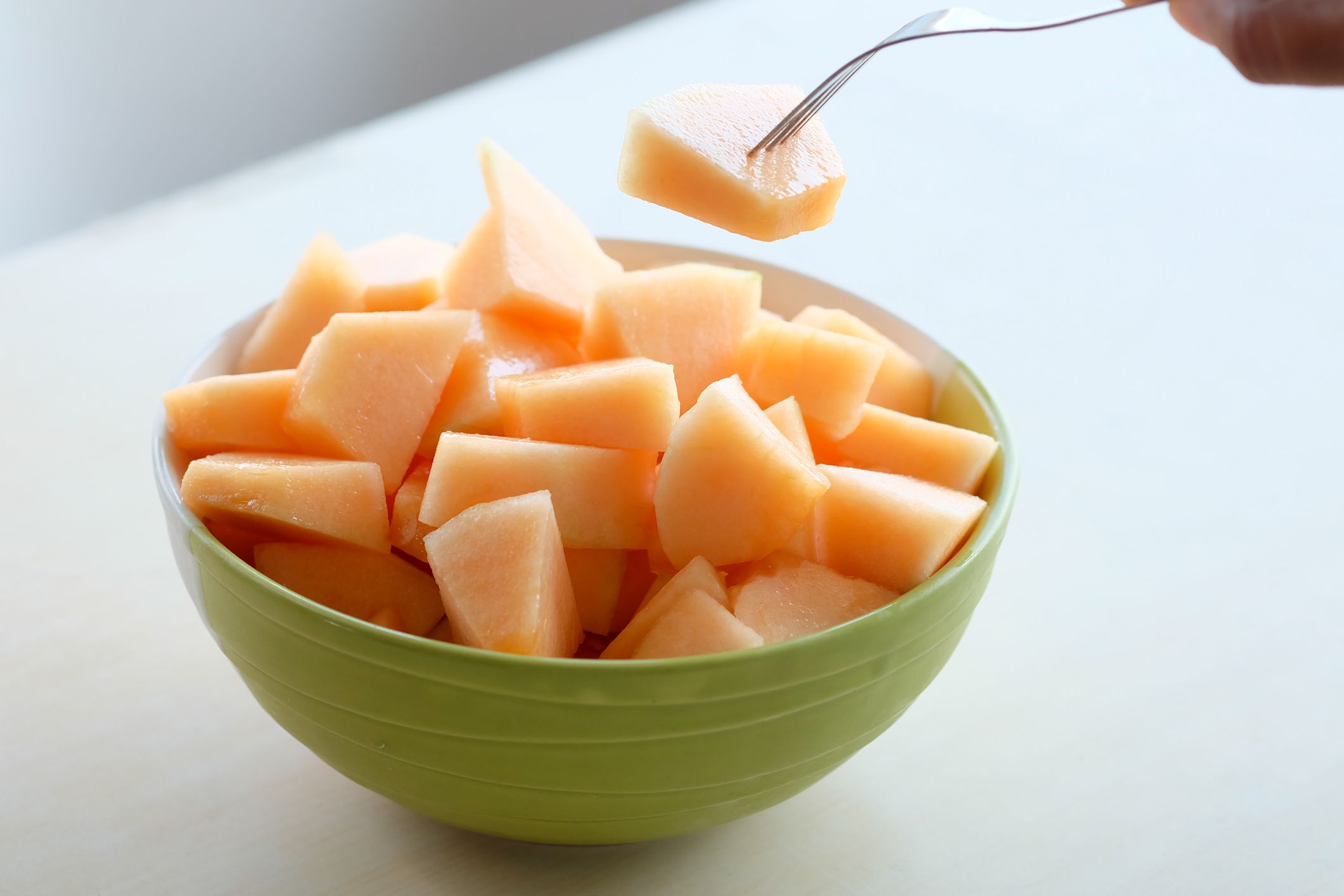The hands of the people are using the fork to melt the orange Melon. Sweet taste Sliced in a ceramic bowl