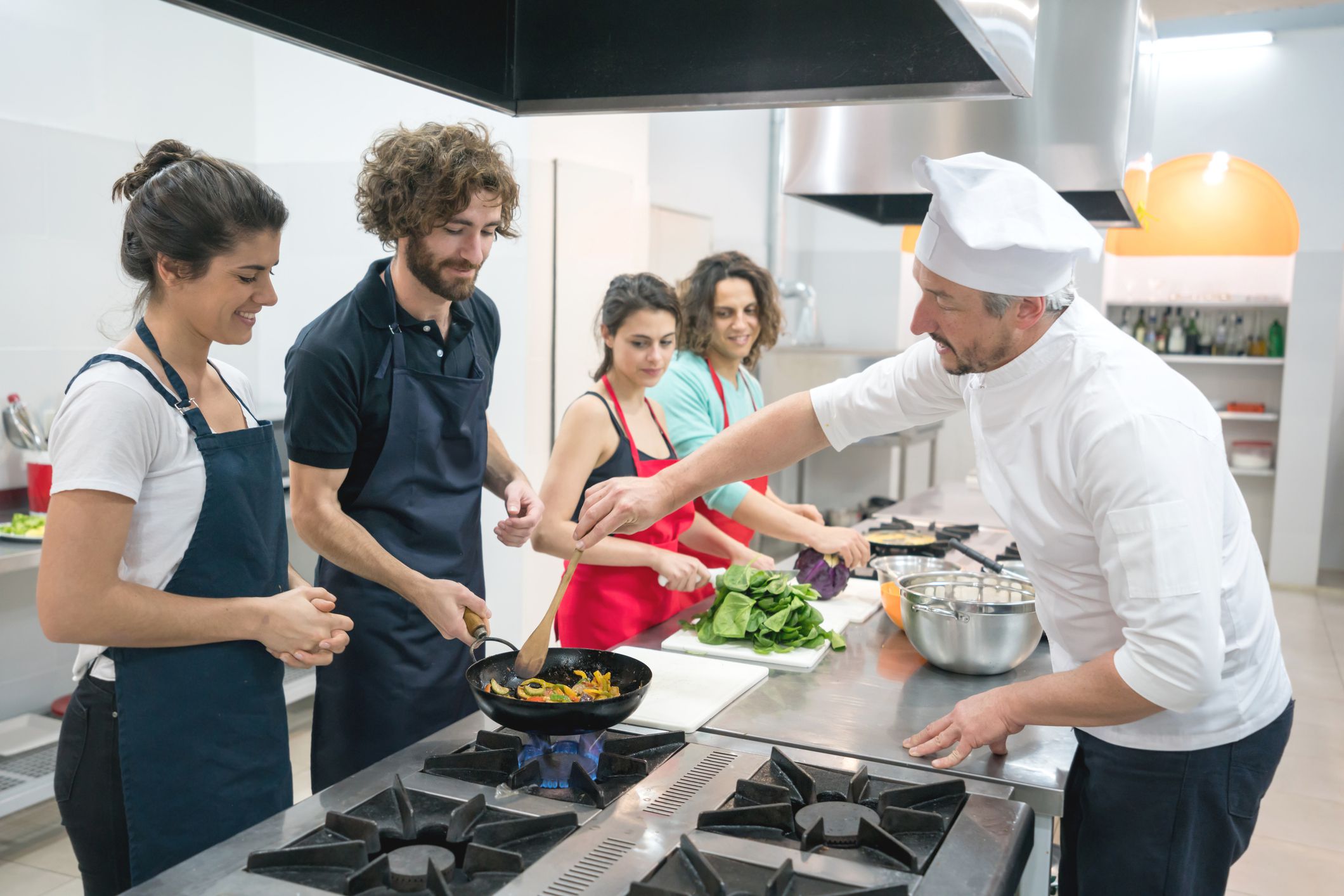 Group of people at a cooking class and chef teaching them how to sauté vegetables on a wok all paying attention and smiling