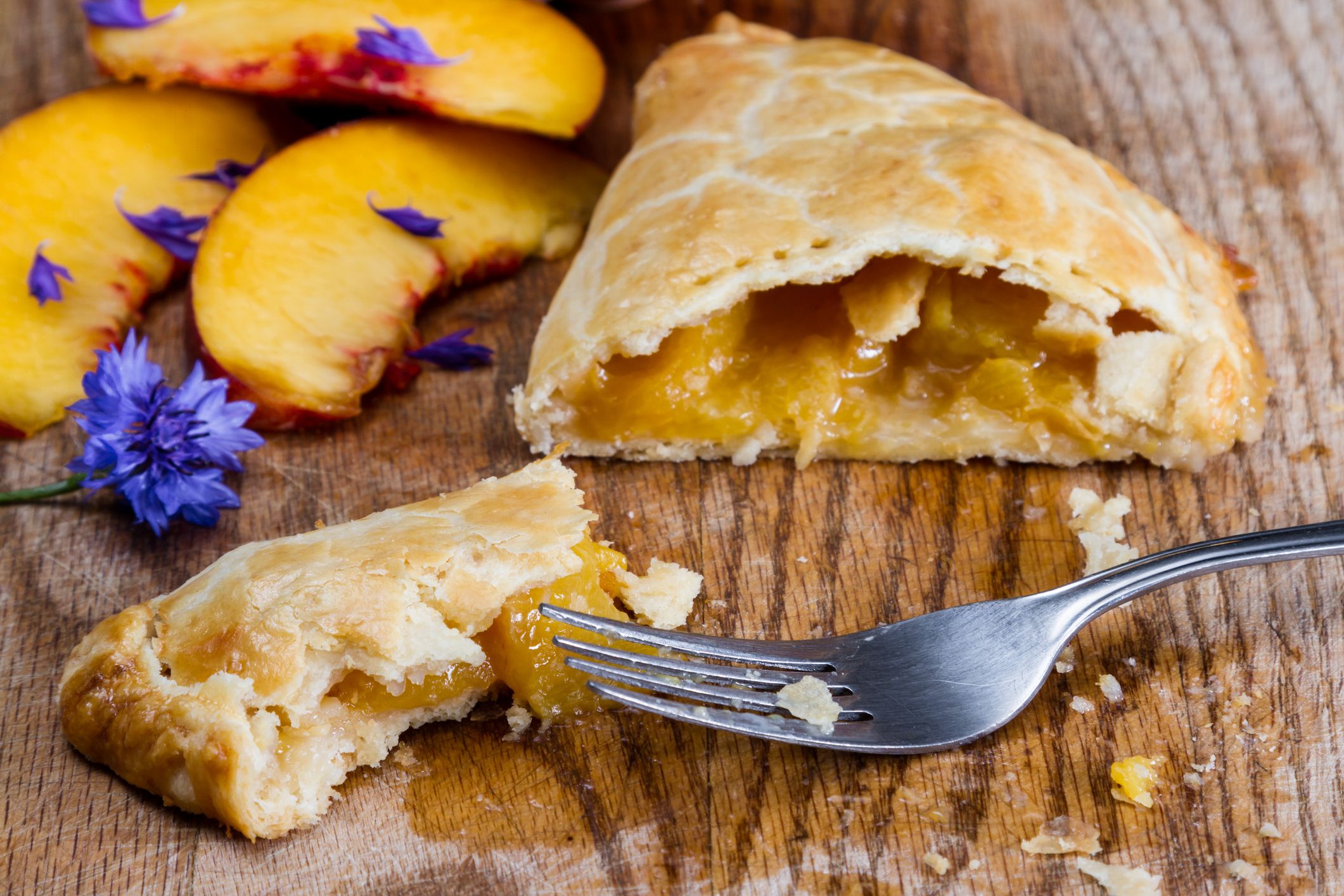 home made peach turnover served on a wooden serving tray with fresh peach slices