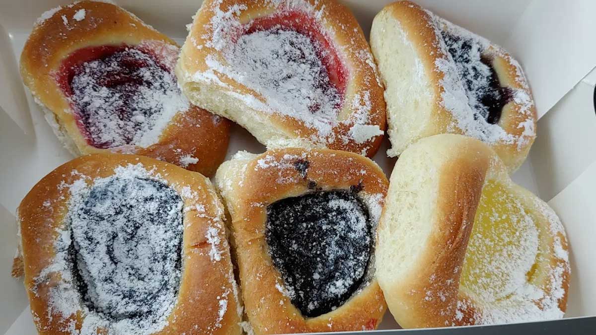 Six kolaches topped with powdered sugar, arranged in a box. With assorted fruity fillings and golden-brown dough, they’re a delicious sample of one of the best breakfast foods in every state.