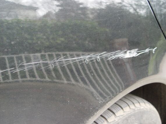 Deep white scratches across the side panel of a dark-colored car.