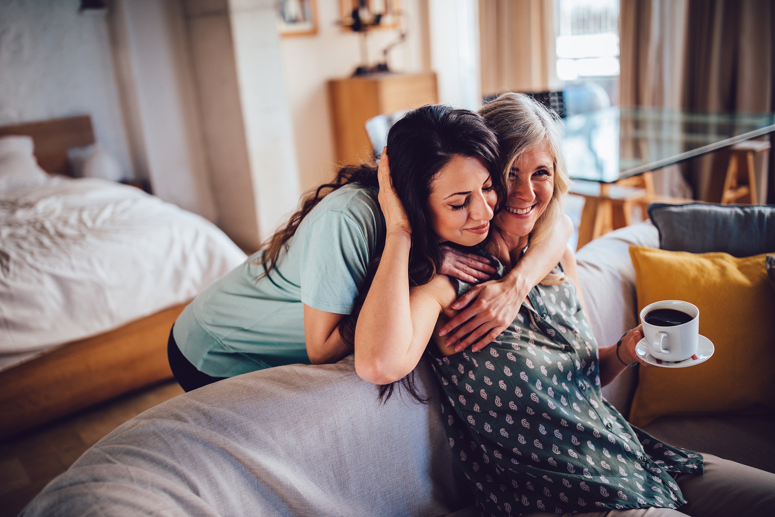 adult daughter embracing smiling senior mother sitting on sofa