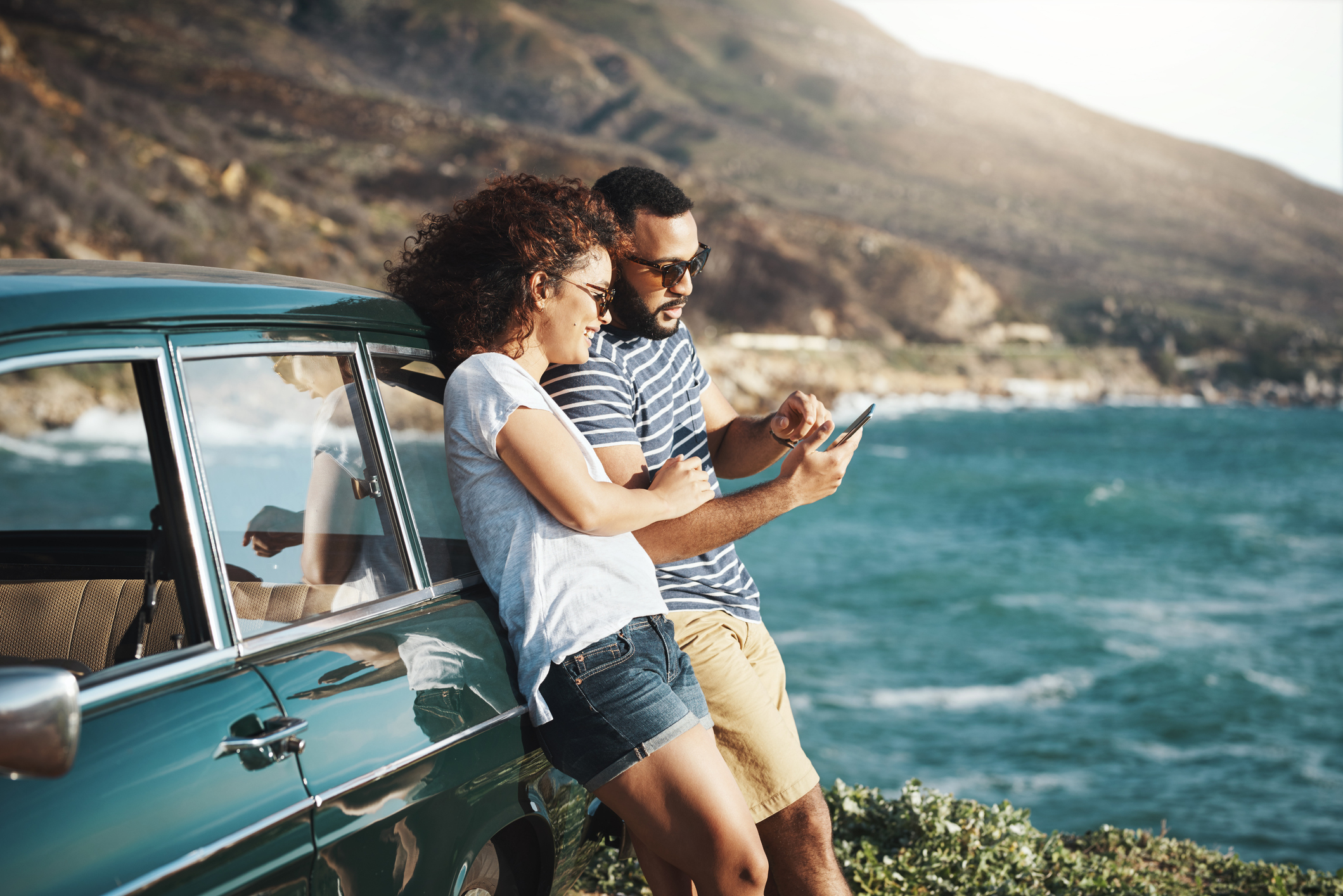 Couple Leaning on Car While Looking at a Smartphone, Parked Outside Along the Coast