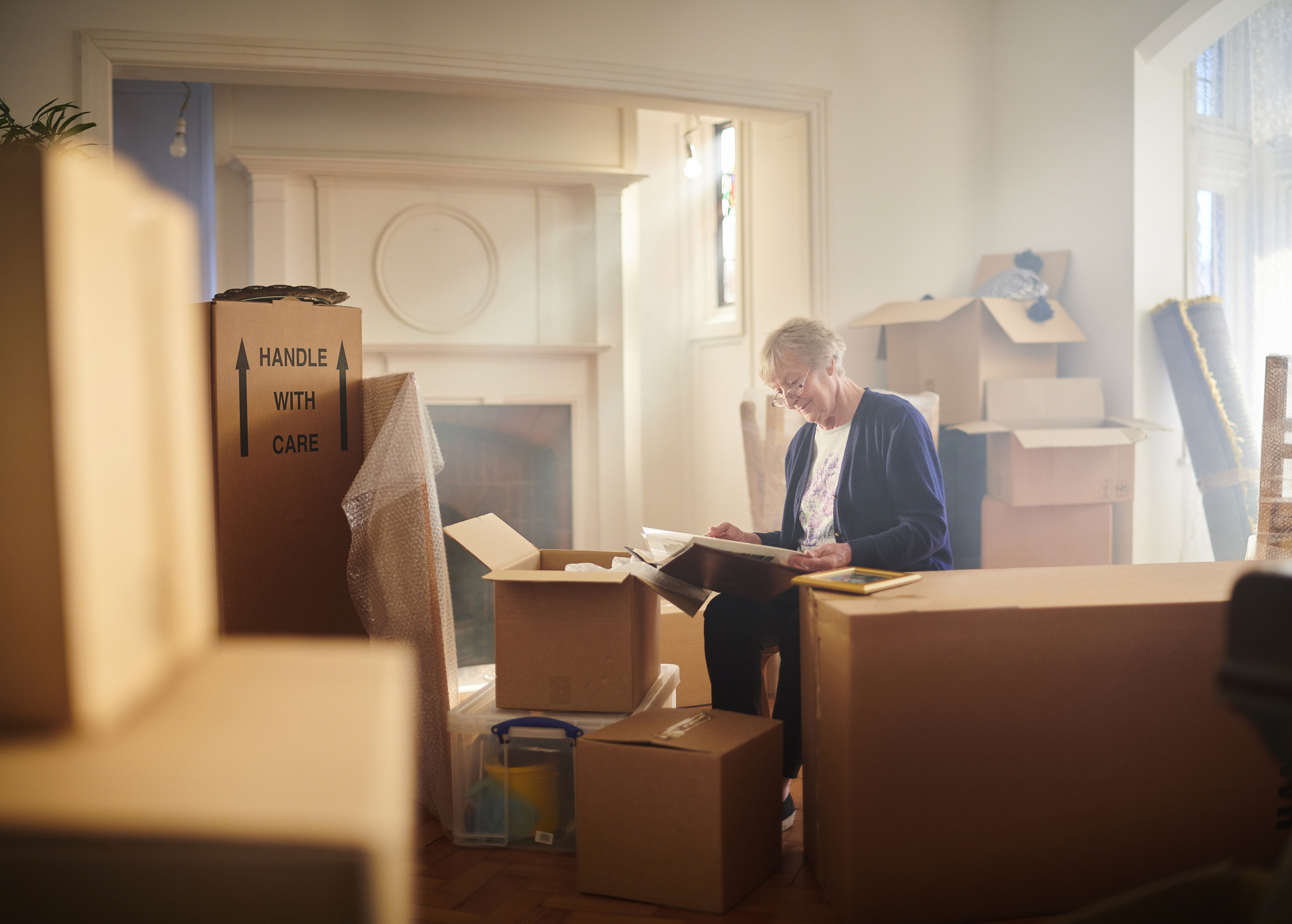 Smiling Senior Woman Looking at Photo Album Among Packed Boxes During a Move