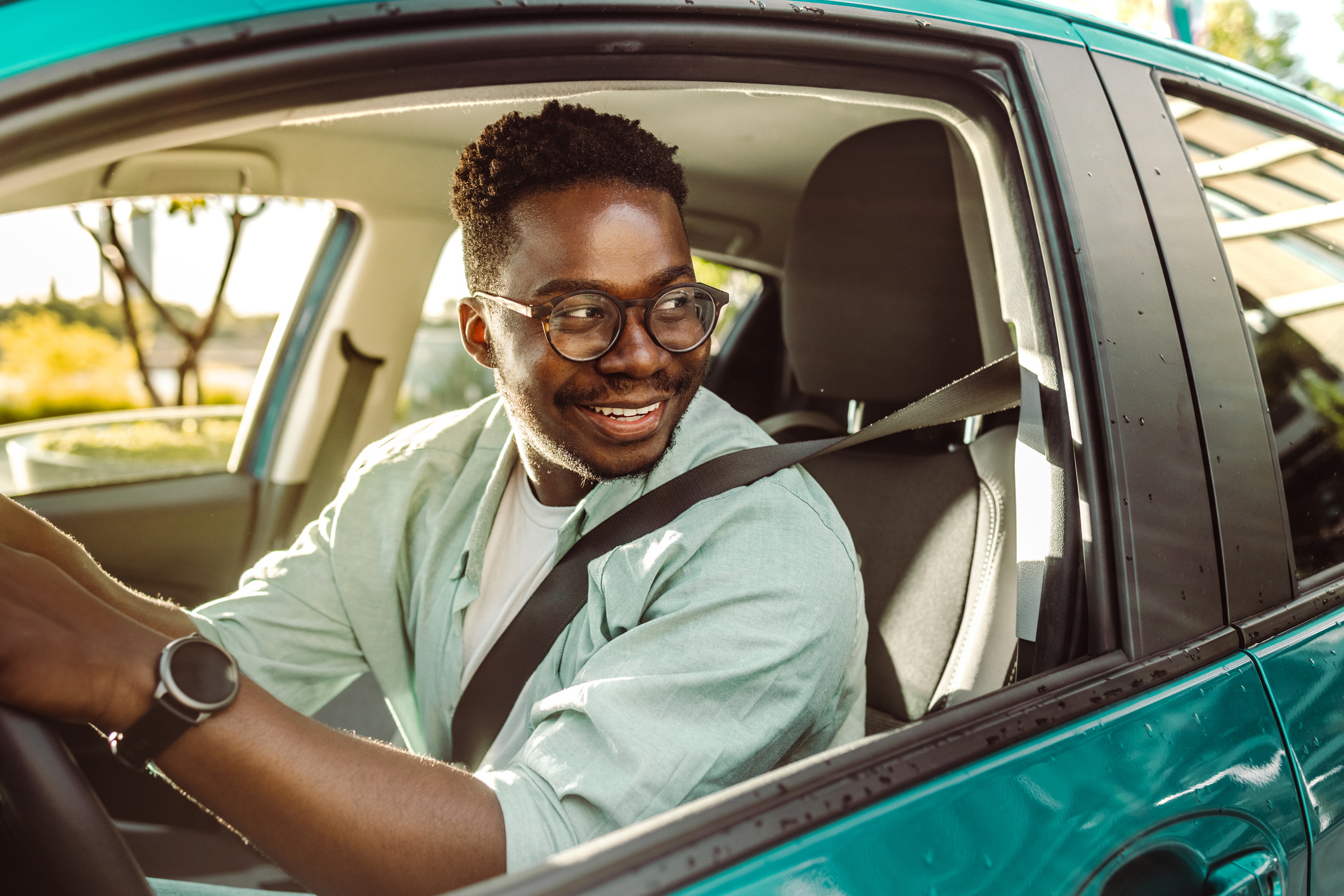 Smiling Man Looking Out of His Window While Driving an Aqua Car