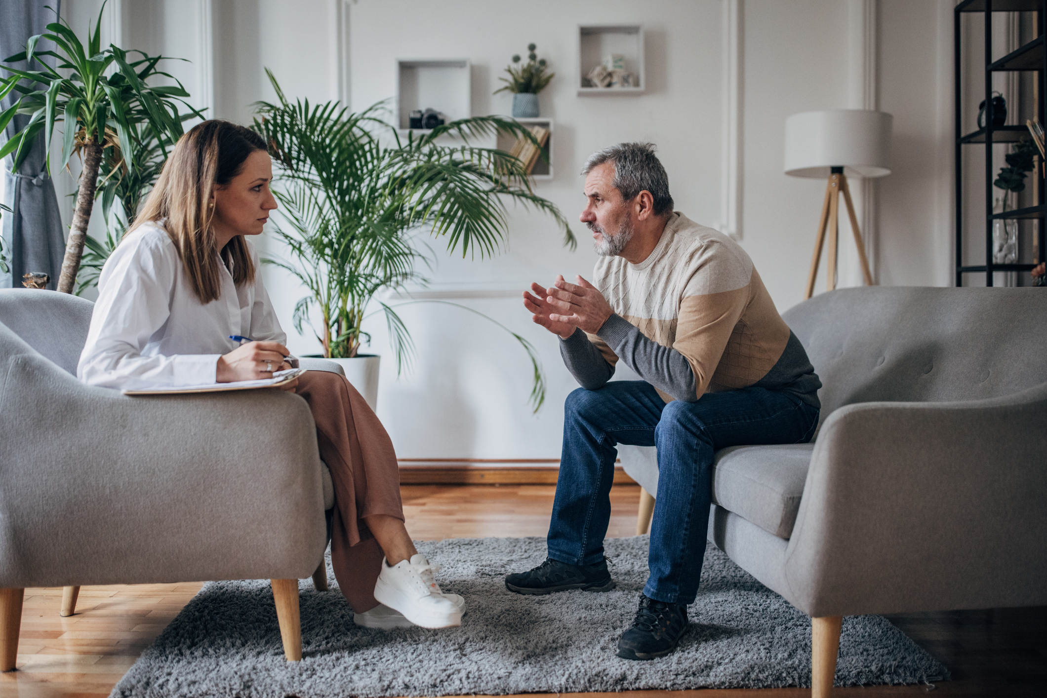 Side-View of Senior Man, Right, Talking to a Female Therapist, Left, in Her Office