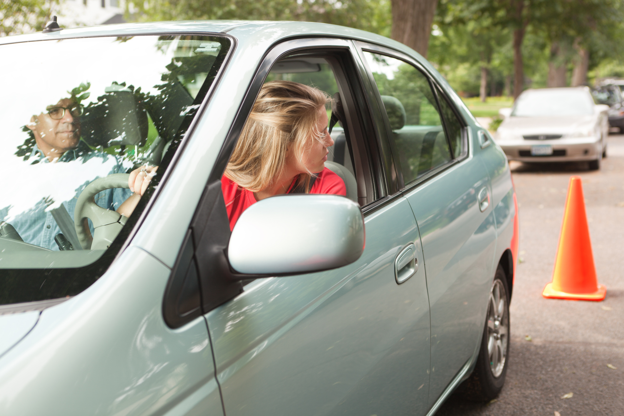 Young Woman Driver Learning Parallel Parking with Driving Instructor and Cone