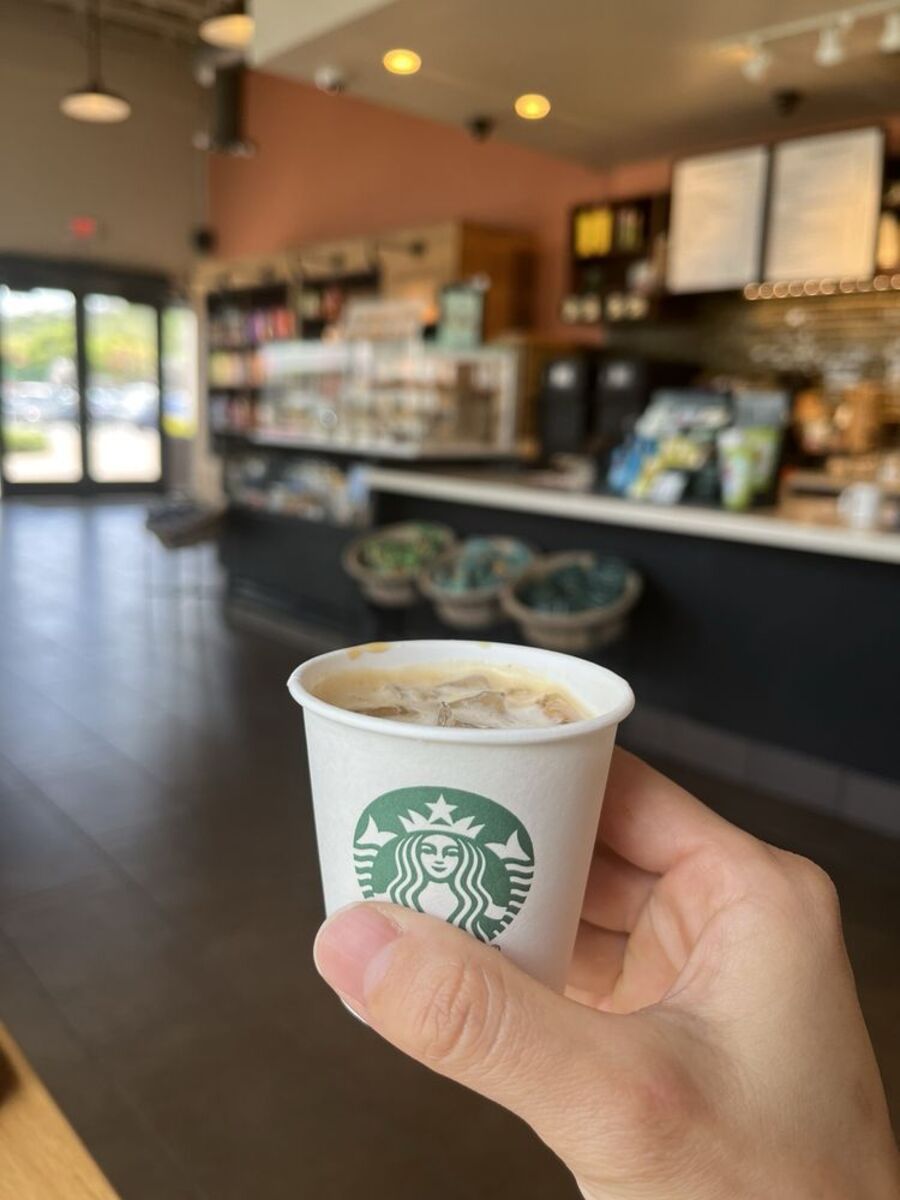 Hand Holding a White Cup of Two Shot of Starbucks Espresso, in Front of Ordering Area