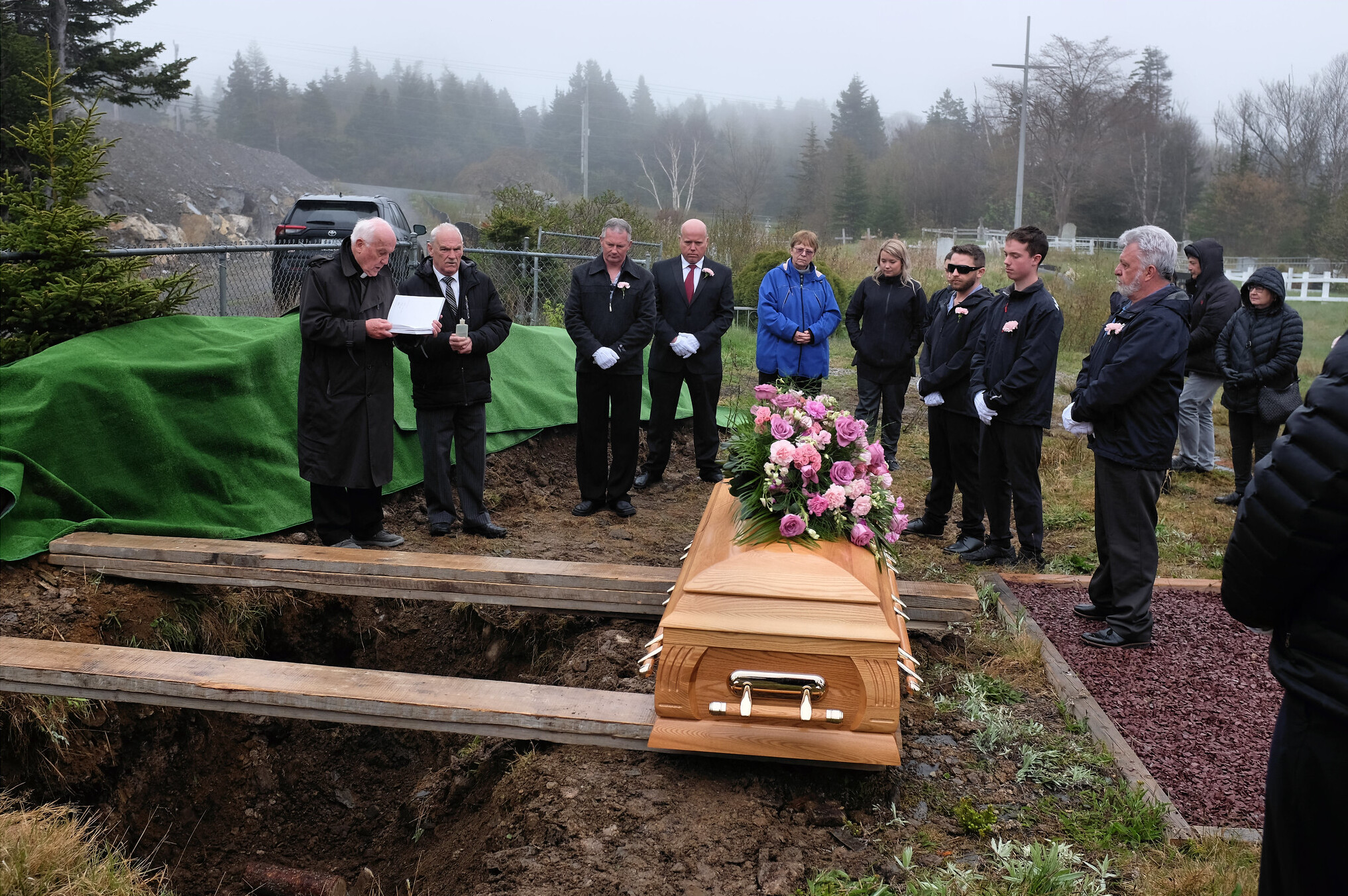 People Attending a Funeral Outside With Light Brown Wooden Casket, Rainy Weather