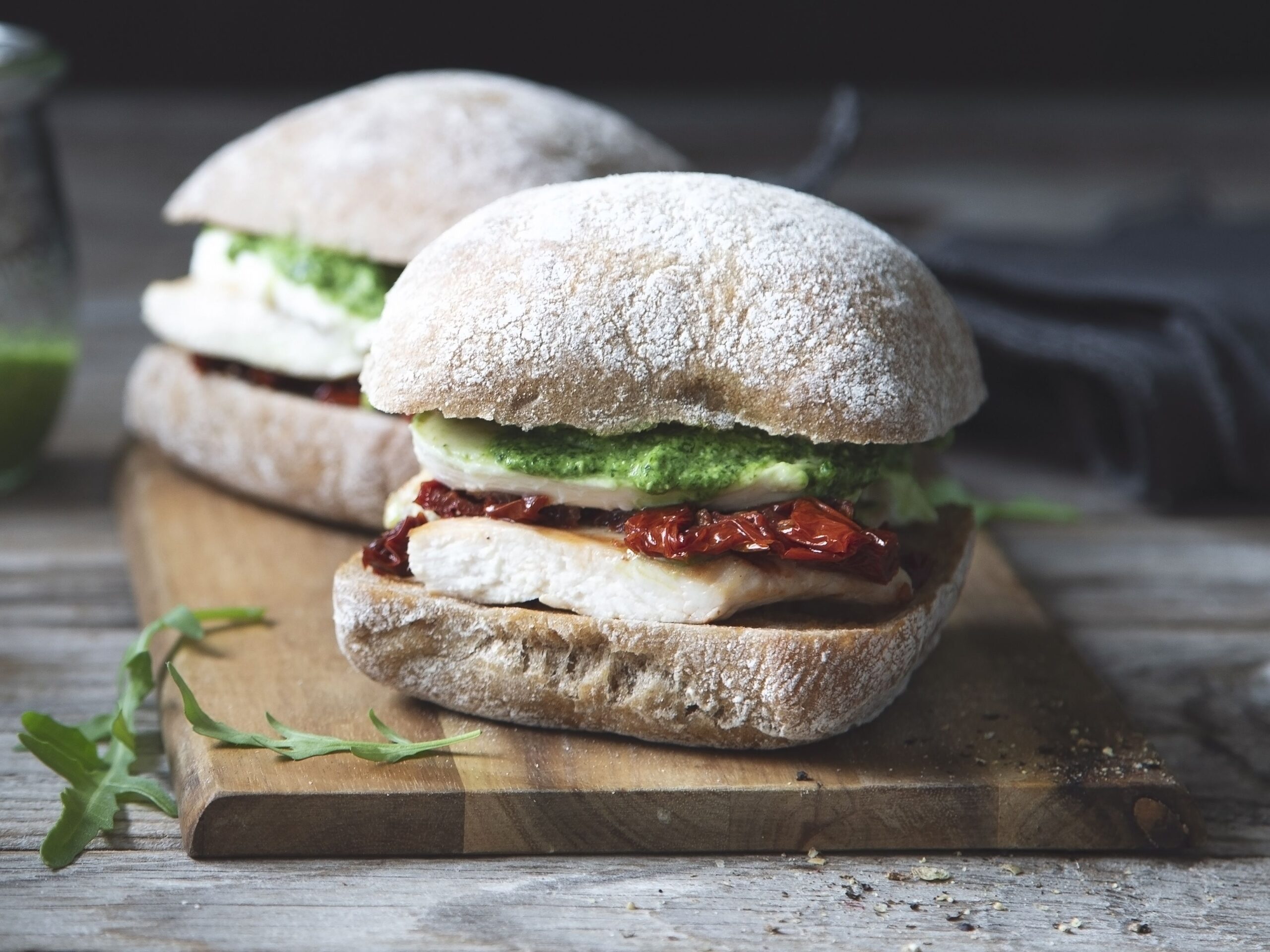Sandwiches with grilled chicken, dried tomatoes, mozzarella and pesto sauce on wooden background. Selective focus. Copy space.