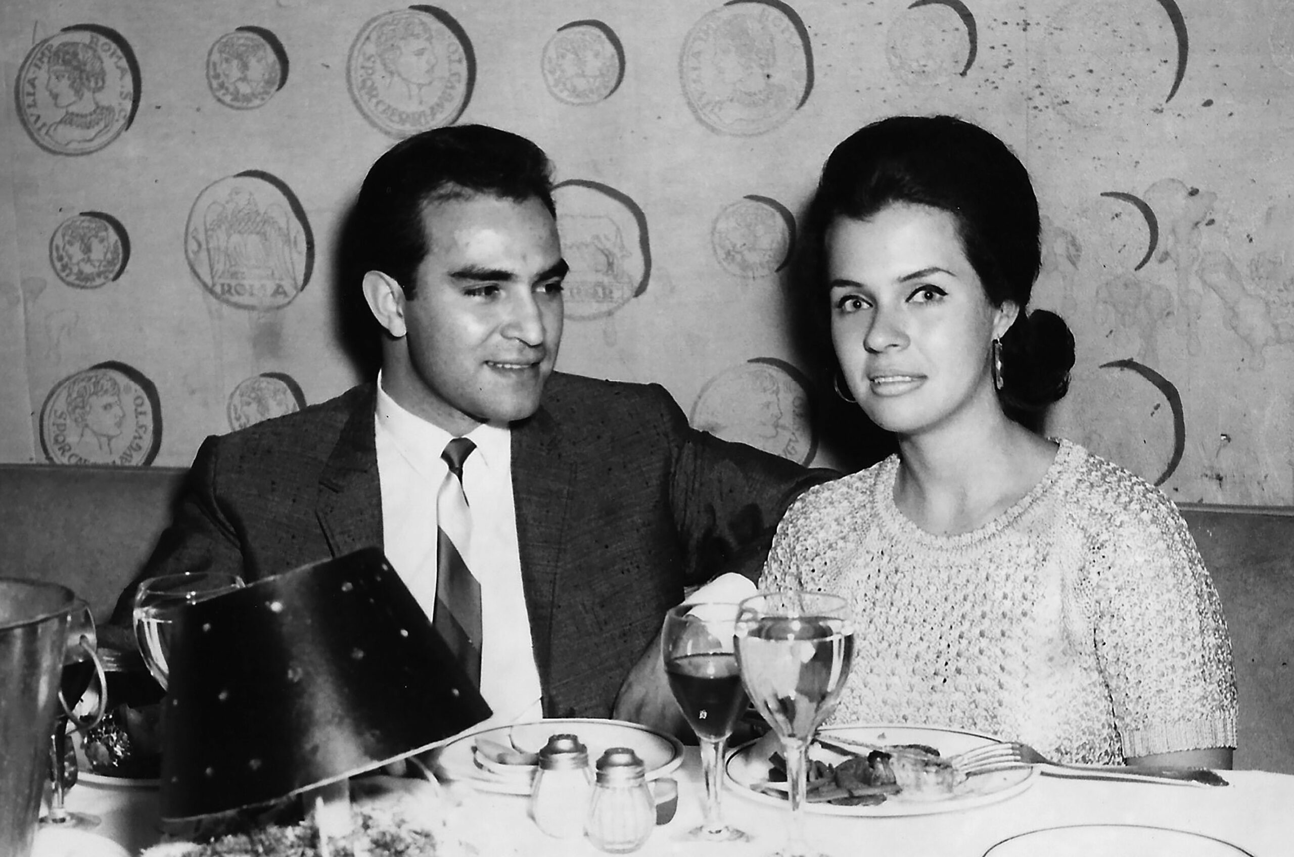 Black and white Image taken in the 60s - hispanic young man posing with his caucasian young girlfriend having dinner sitting in a restaurant table