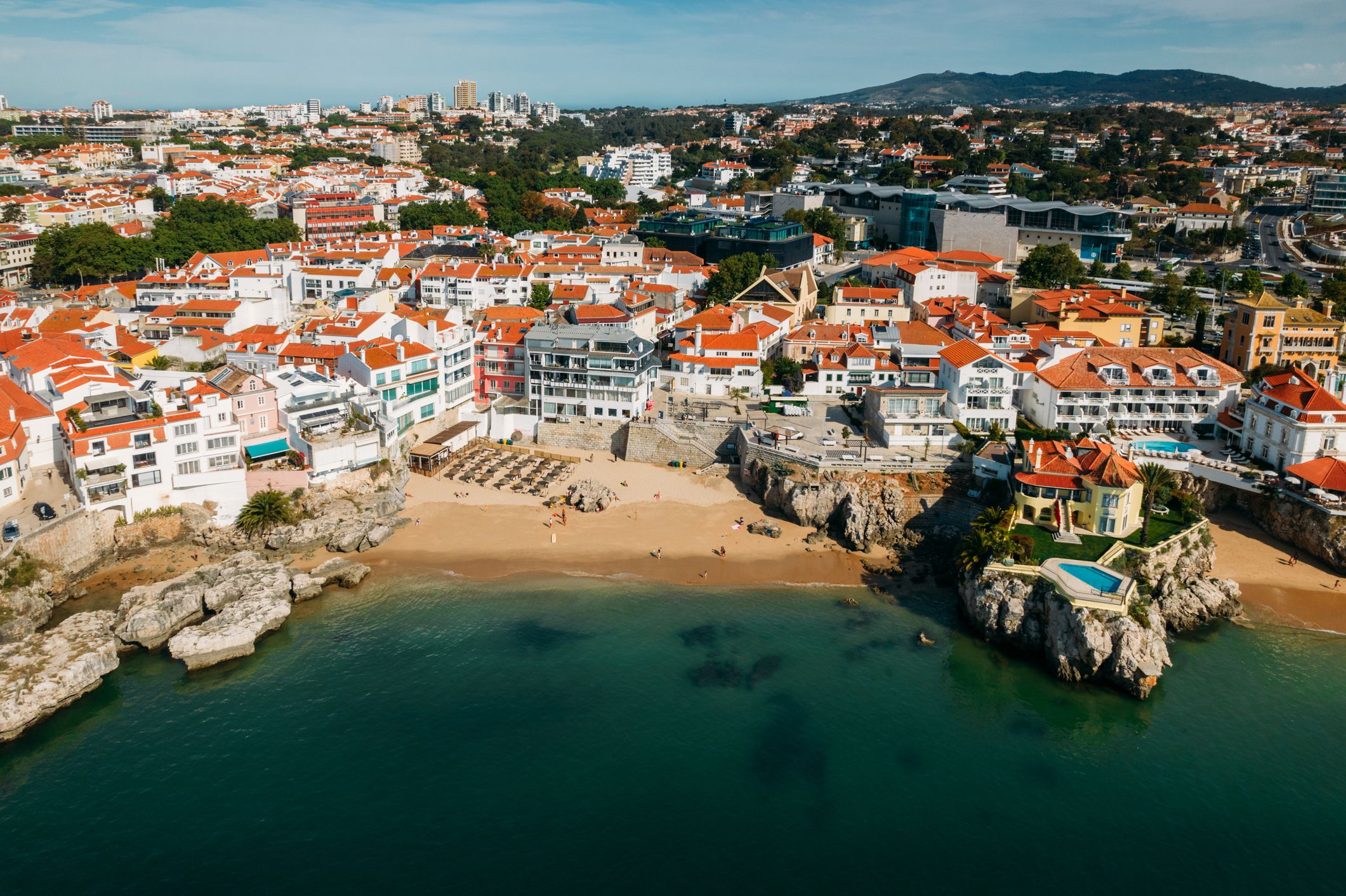 Drone aerial view of unidentifiable sunbathers at Praia da Rainha beach in Cascais, Portugal, a popular summer vacation spot for Portuguese and foreign tourists