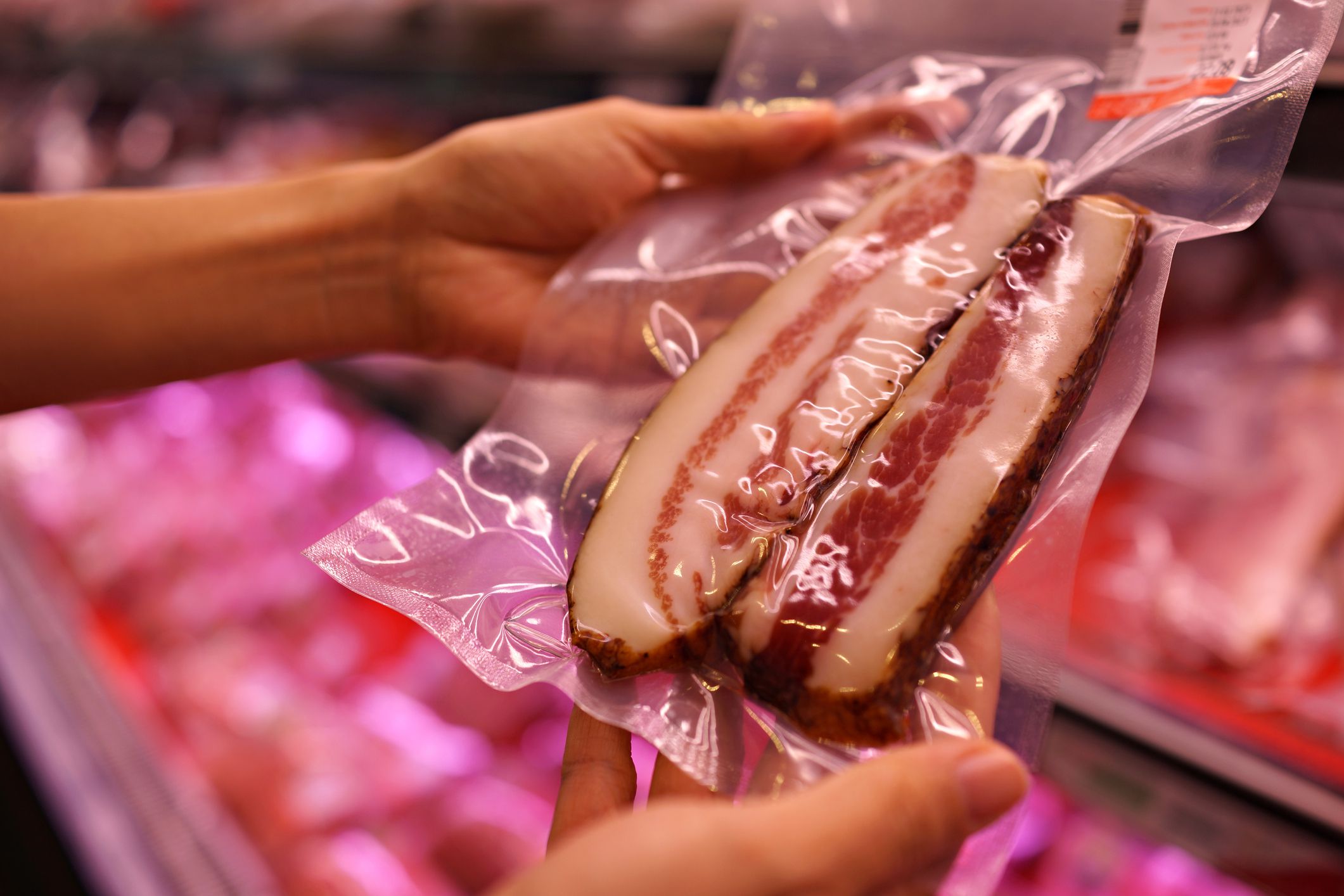 Cropped shot of woman choosing Italian bacon at processed meat section in the supermarket.
