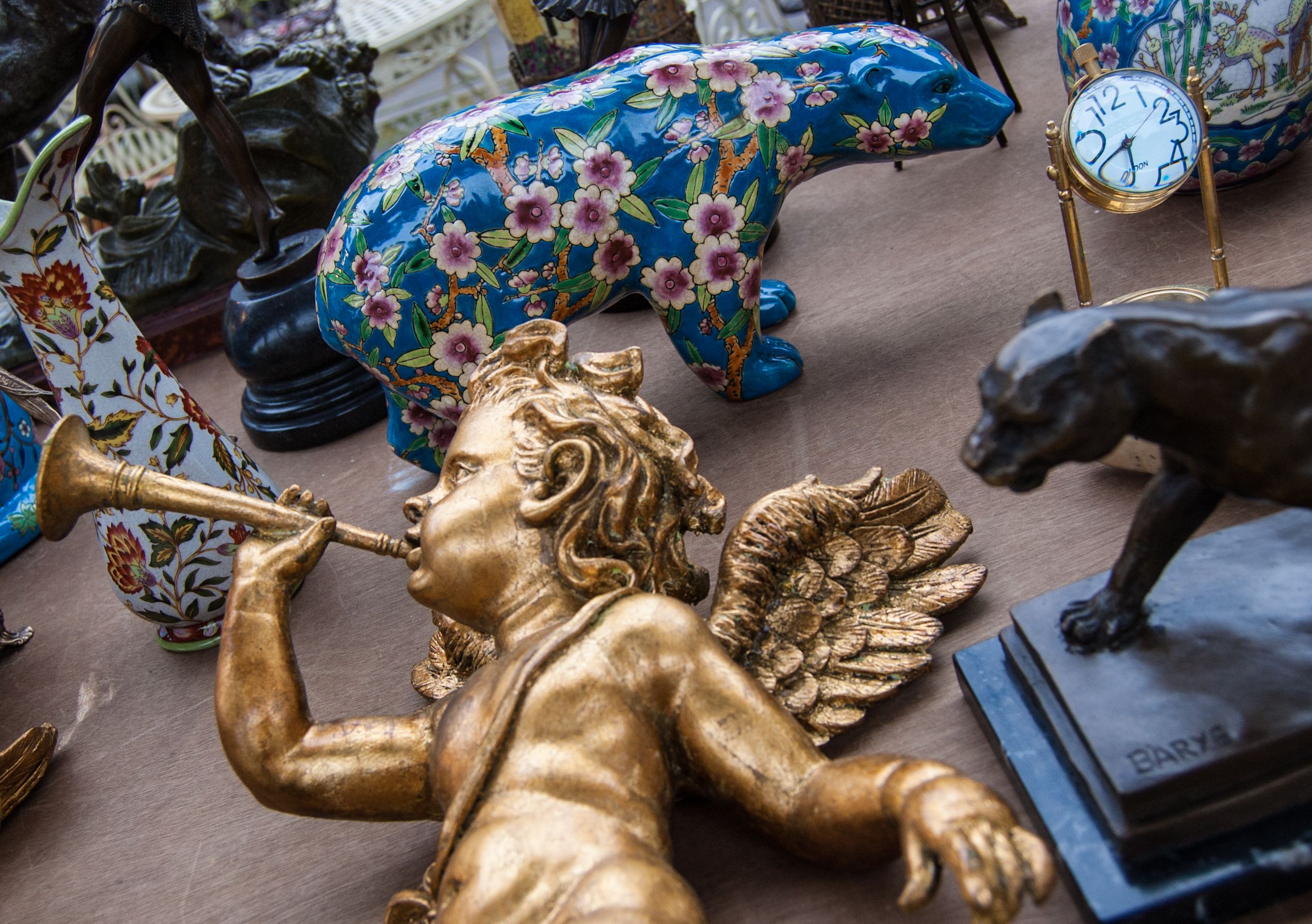 Golden baby angel playing on trumpet. Colorful bear figurine at background. Flea market.