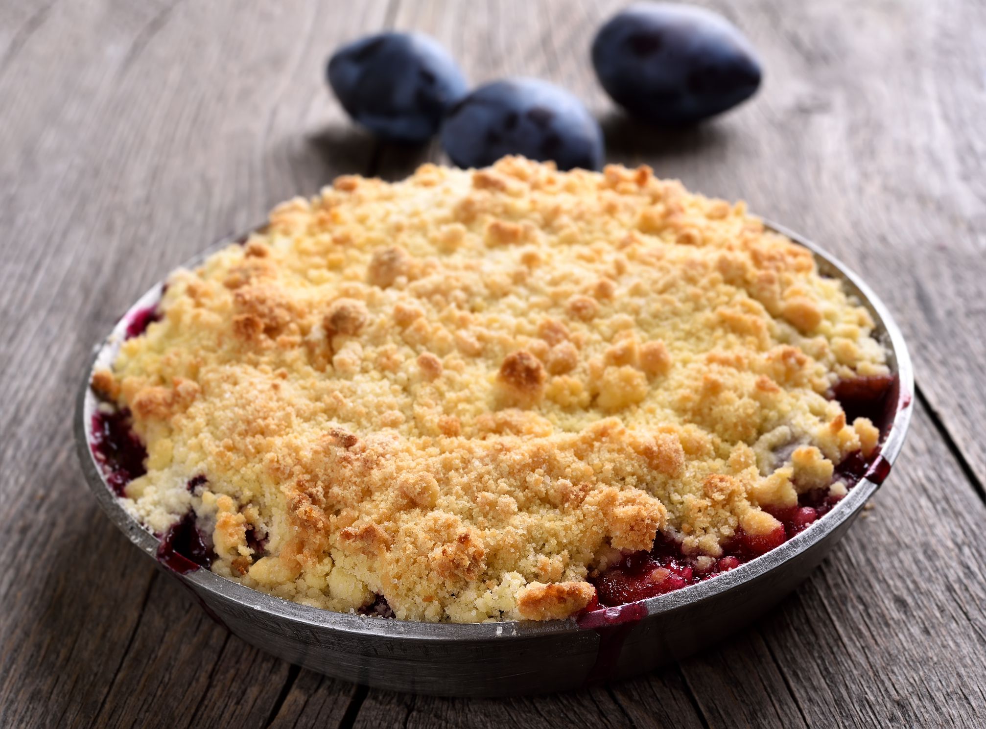 Plum crumb pie in pan on wooden background