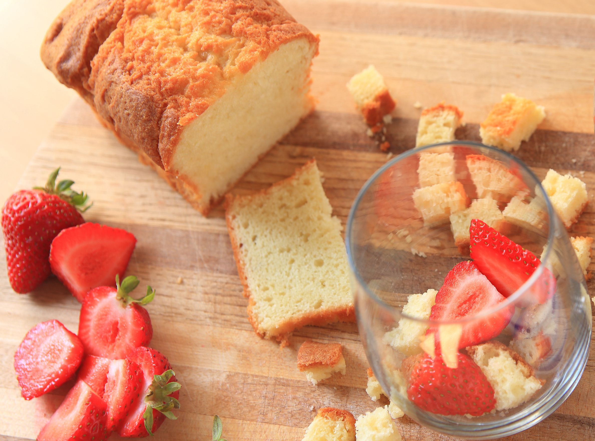 Overhead of strawberries, whipped cream and pound cake with finished miniature trifle on cutting board